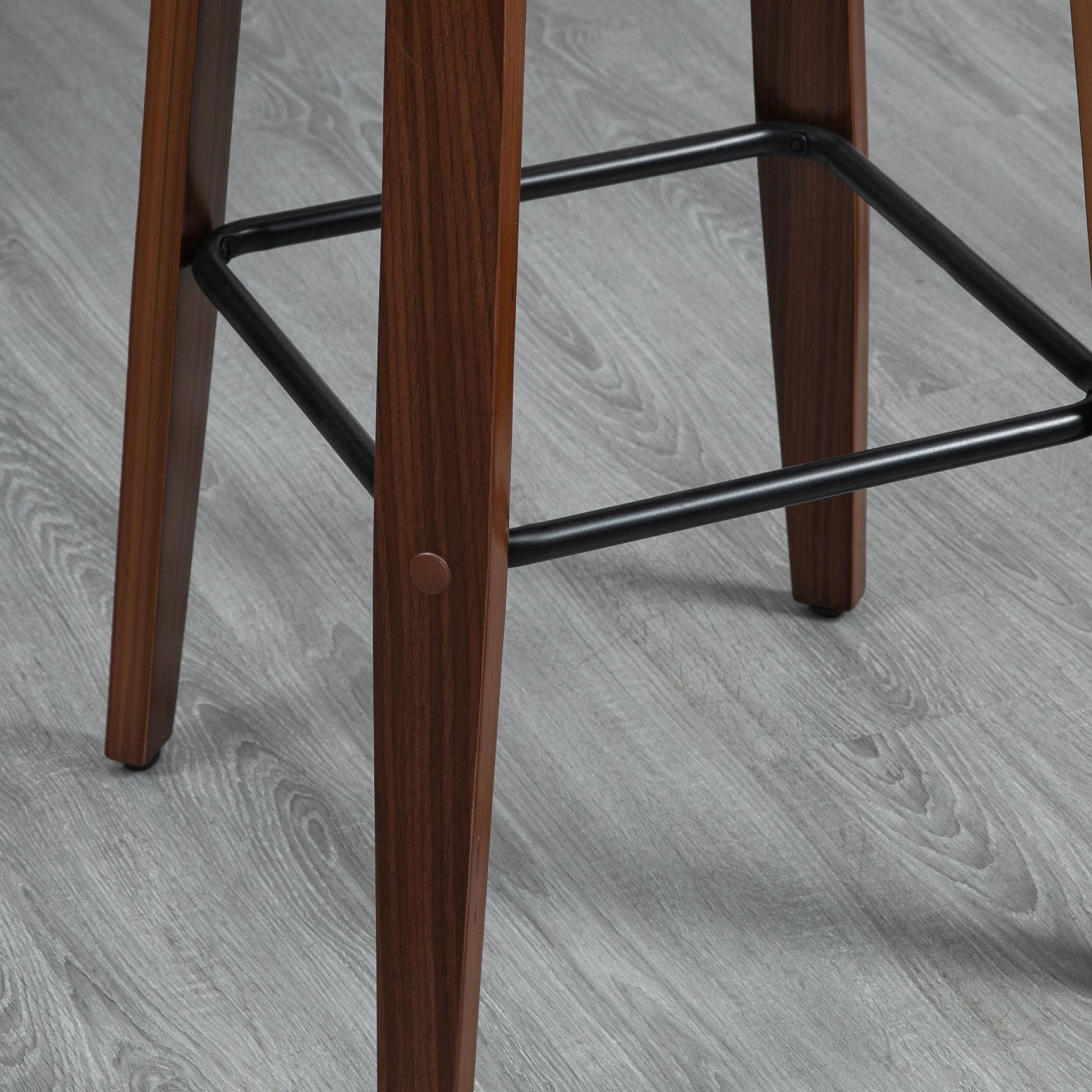 Wooden bar stool legs with black metal footrest detail on gray floor