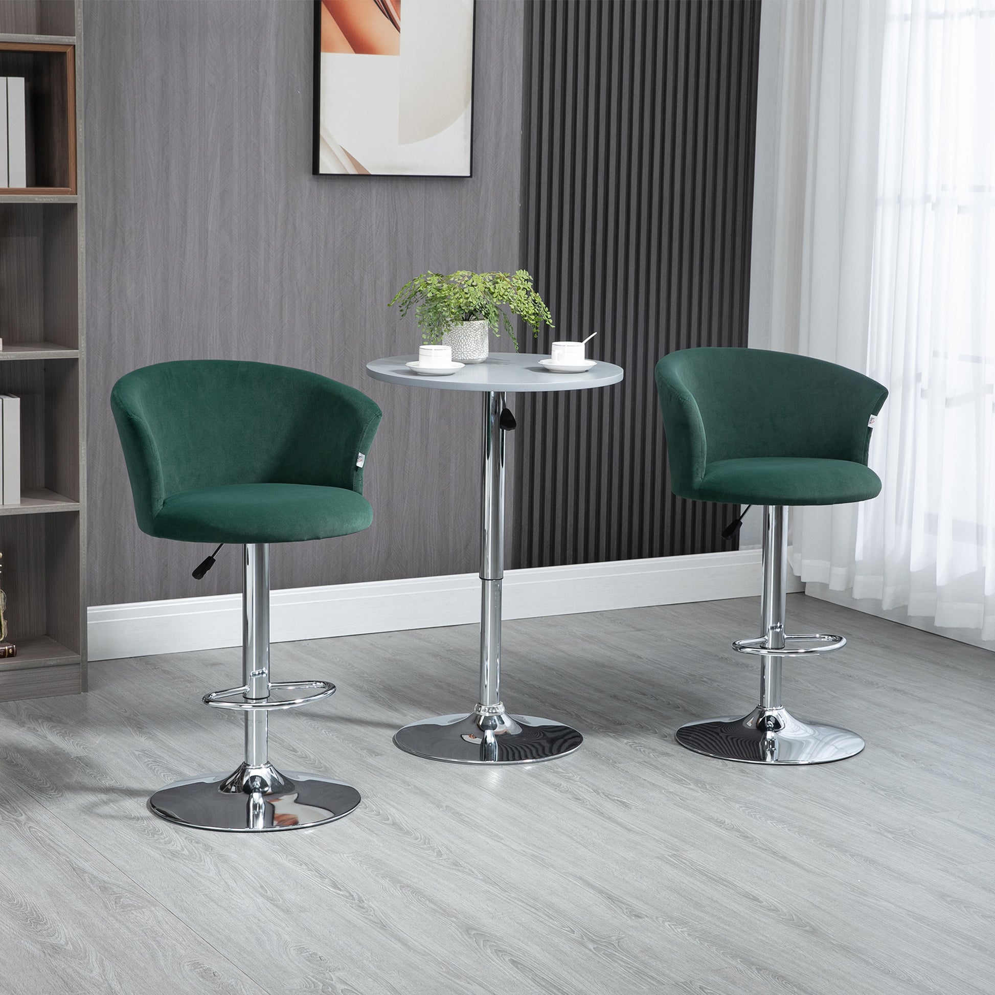 Two dark green velvet bar stools with chrome bases flank a gray adjustable height pub table