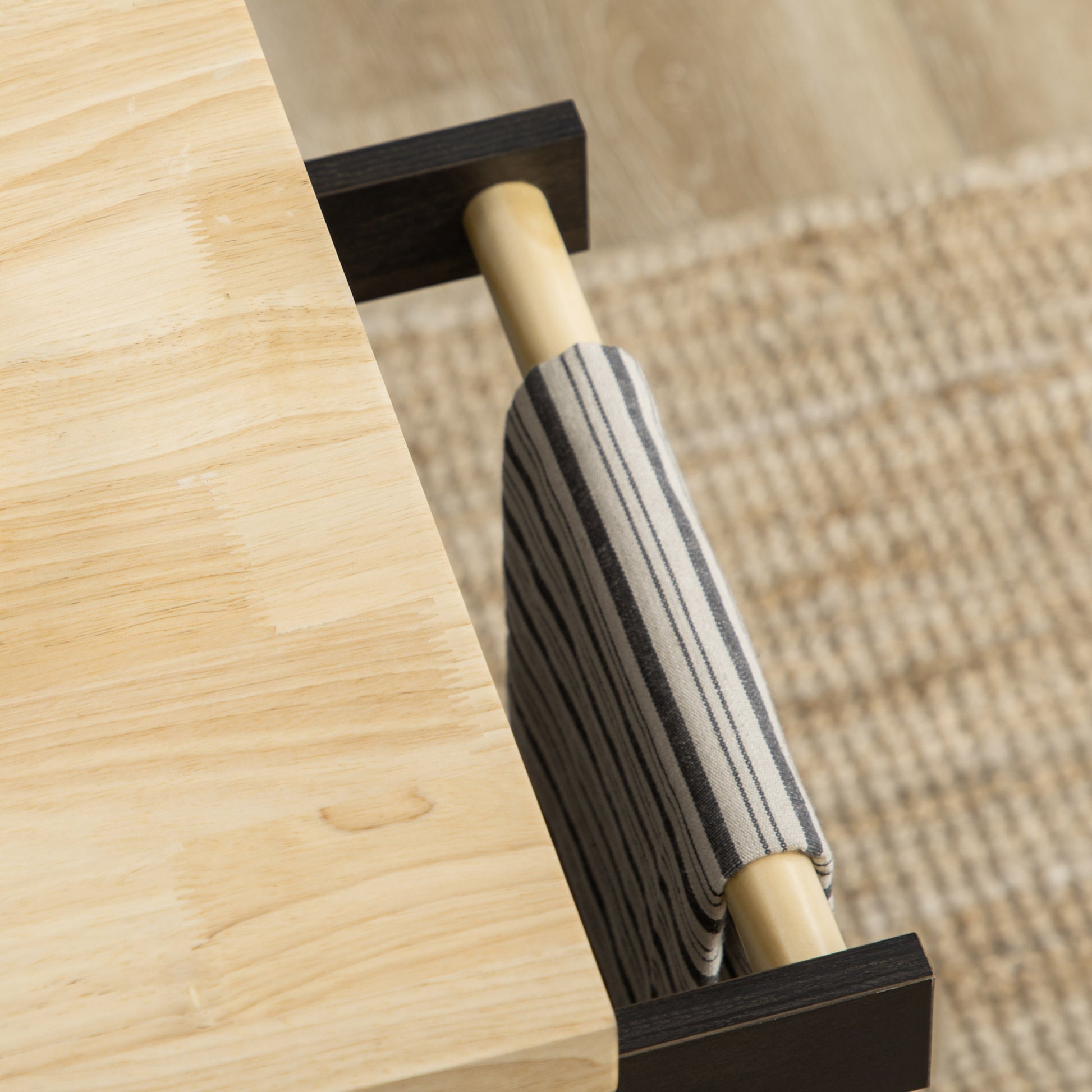 Light wood desk surface detail with dark wood leg and striped fabric accent