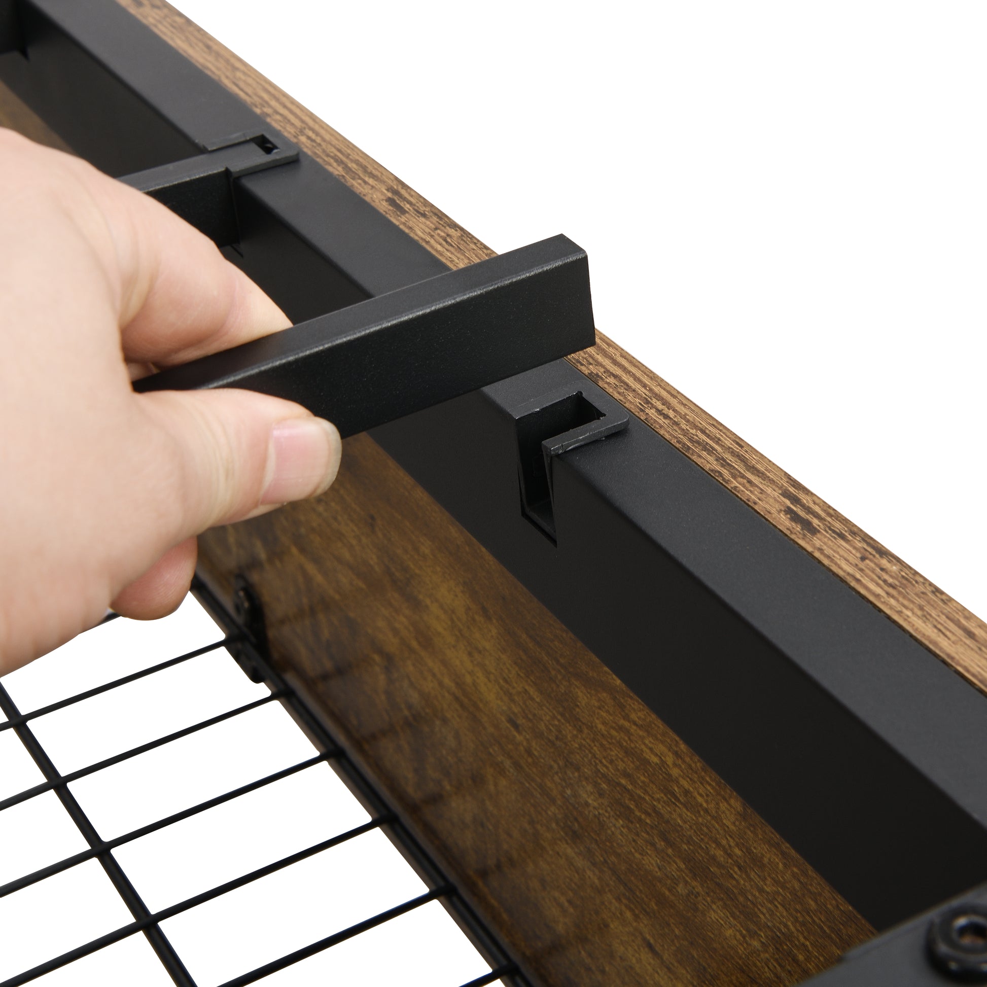 Closeup of a hand attaching a black metal bracket to a rustic wood shelf showcasing its sturdy construction