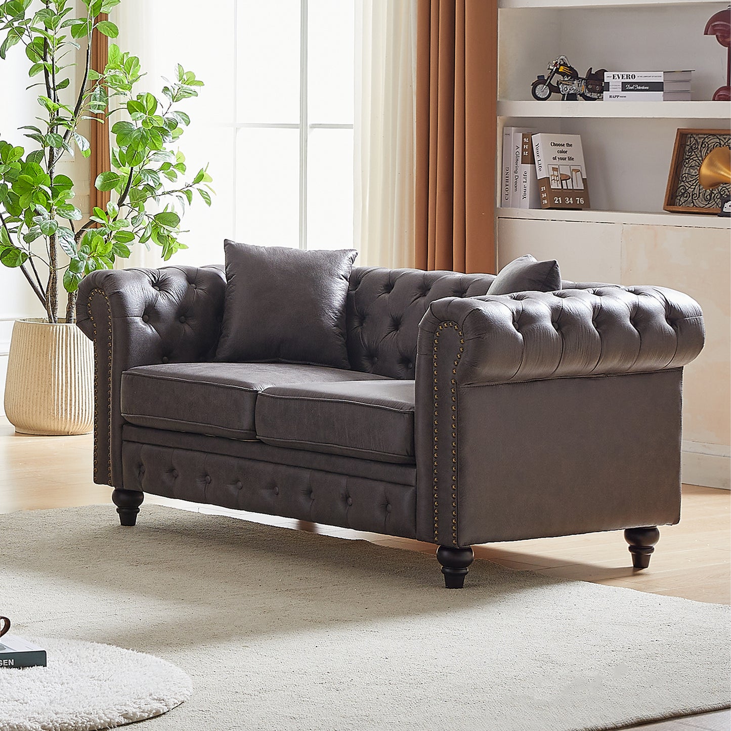 Dark brown tufted leather chesterfield loveseat with brass nailhead trim and plush pillows