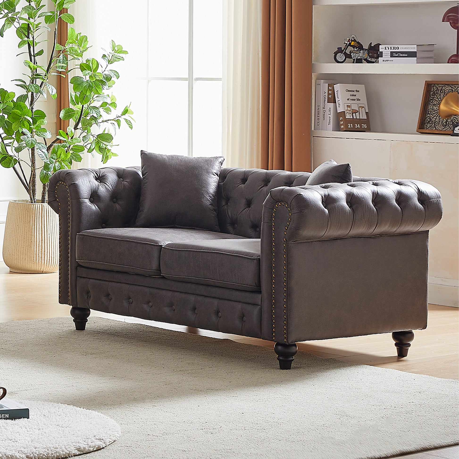 Dark brown tufted leather chesterfield loveseat with brass nailhead trim and plush pillows