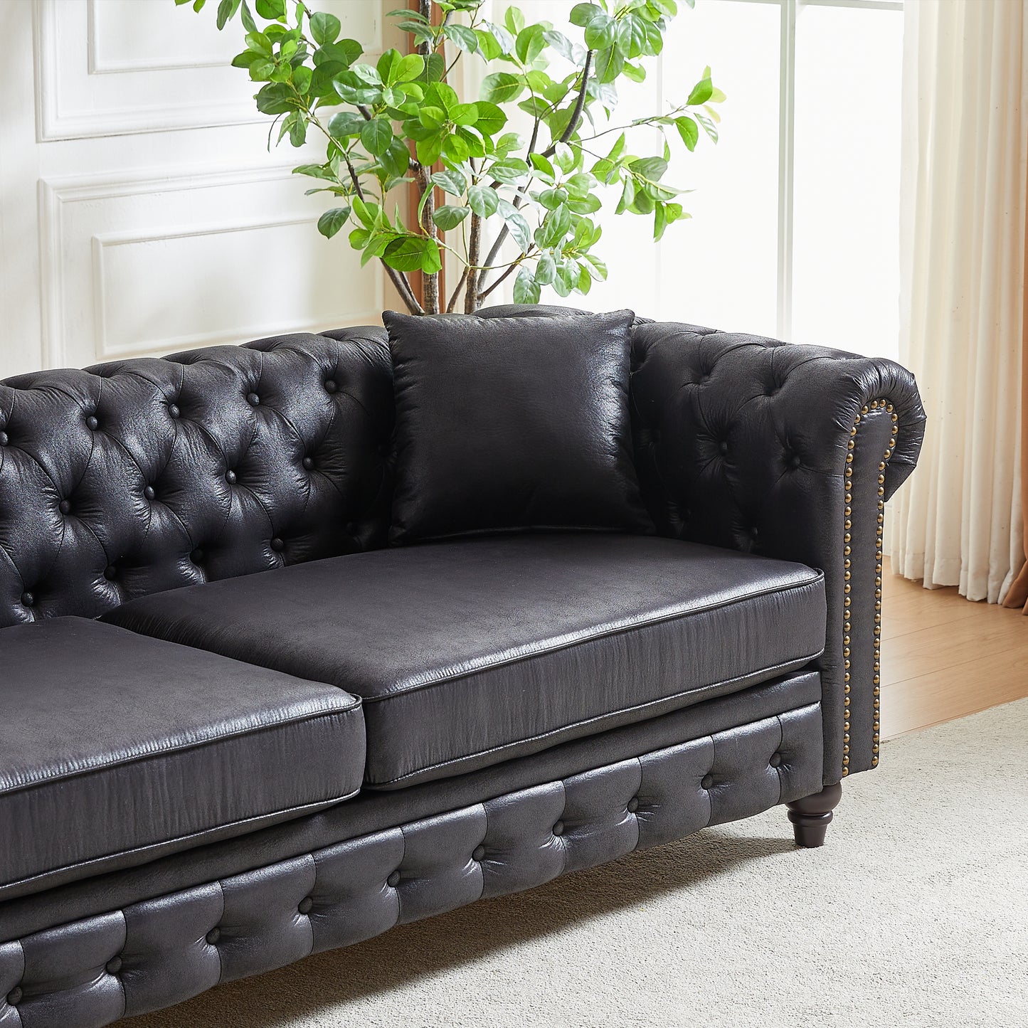 Tufted black leather sofa with decorative brass nailhead trim and plush cushions