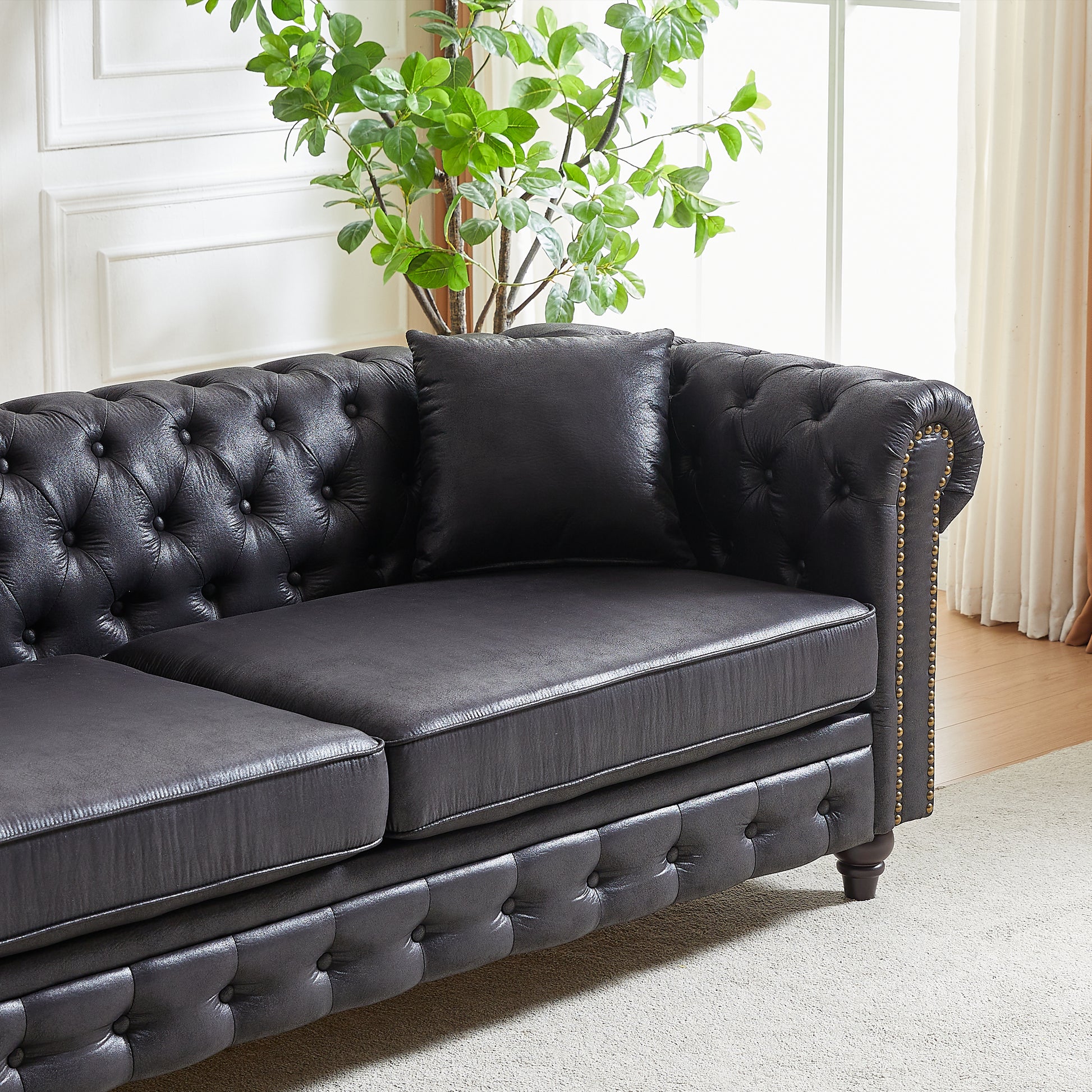 Tufted black leather sofa with decorative brass nailhead trim and plush cushions