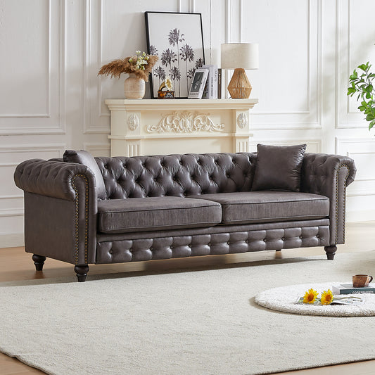Dark grey tufted leather chesterfield sofa with brass nailhead trim and rolled arms