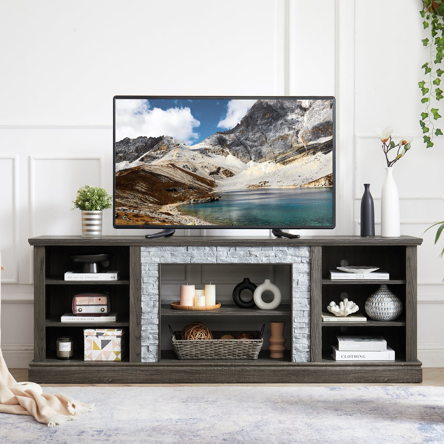 Dark gray media console with faux stone fireplace detail and shelves displaying decor