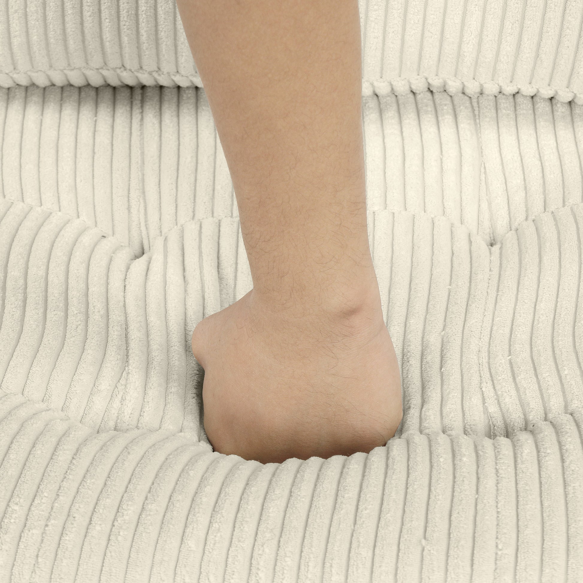 Closeup of a beige corduroy sofa cushion with a hand pressing into its plush texture