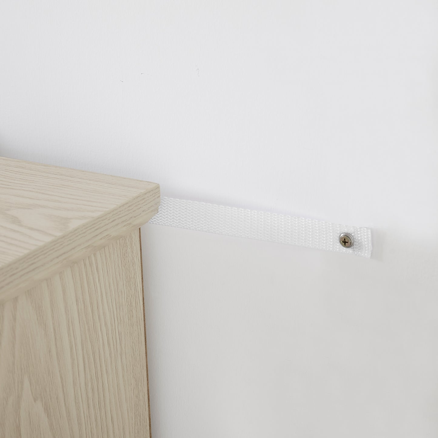 White nylon furniture antitip strap securing light wood cabinet to wall
