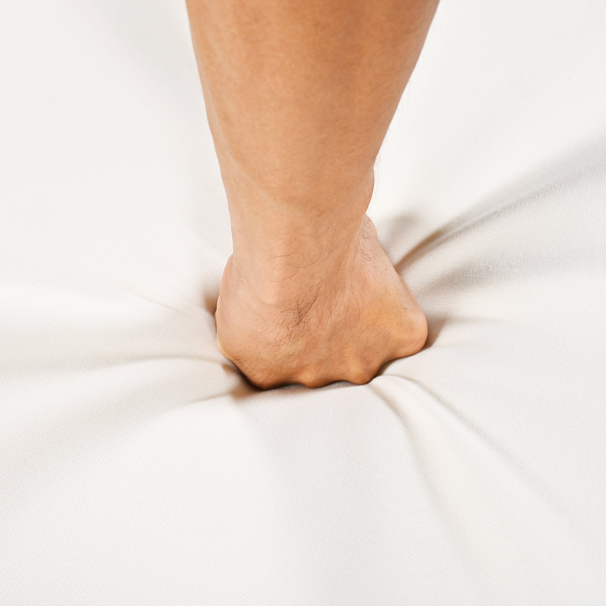 Human foot pressing into plush white mattress showing comfort and support