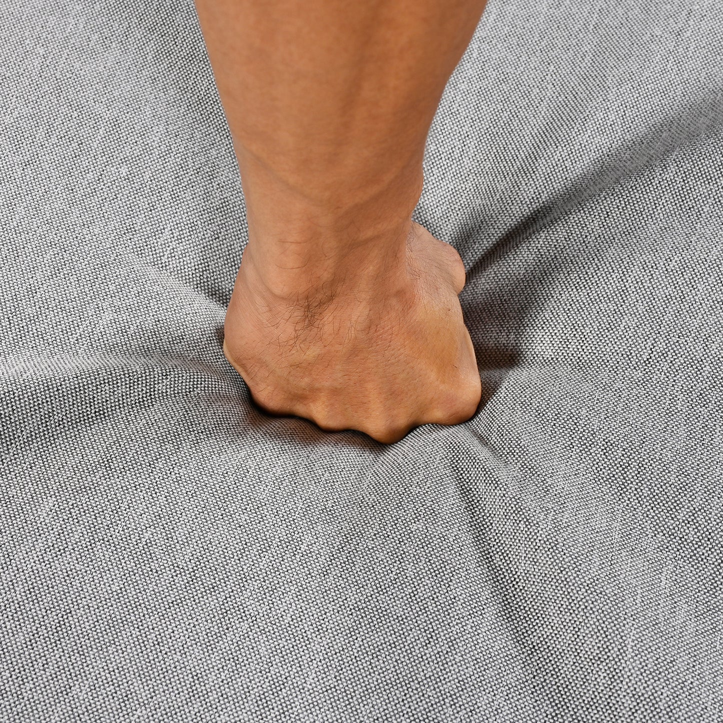 Closeup of a foot pressing into plush grey fabric showing mattress comfort