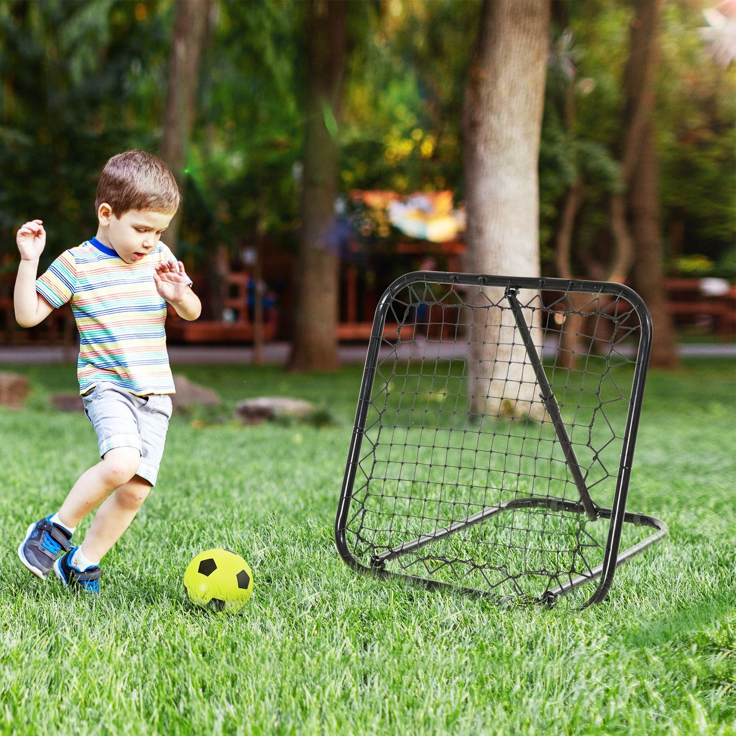 Young boy in striped shirt kicks yellow soccer ball towards a black rebounder net on grass
