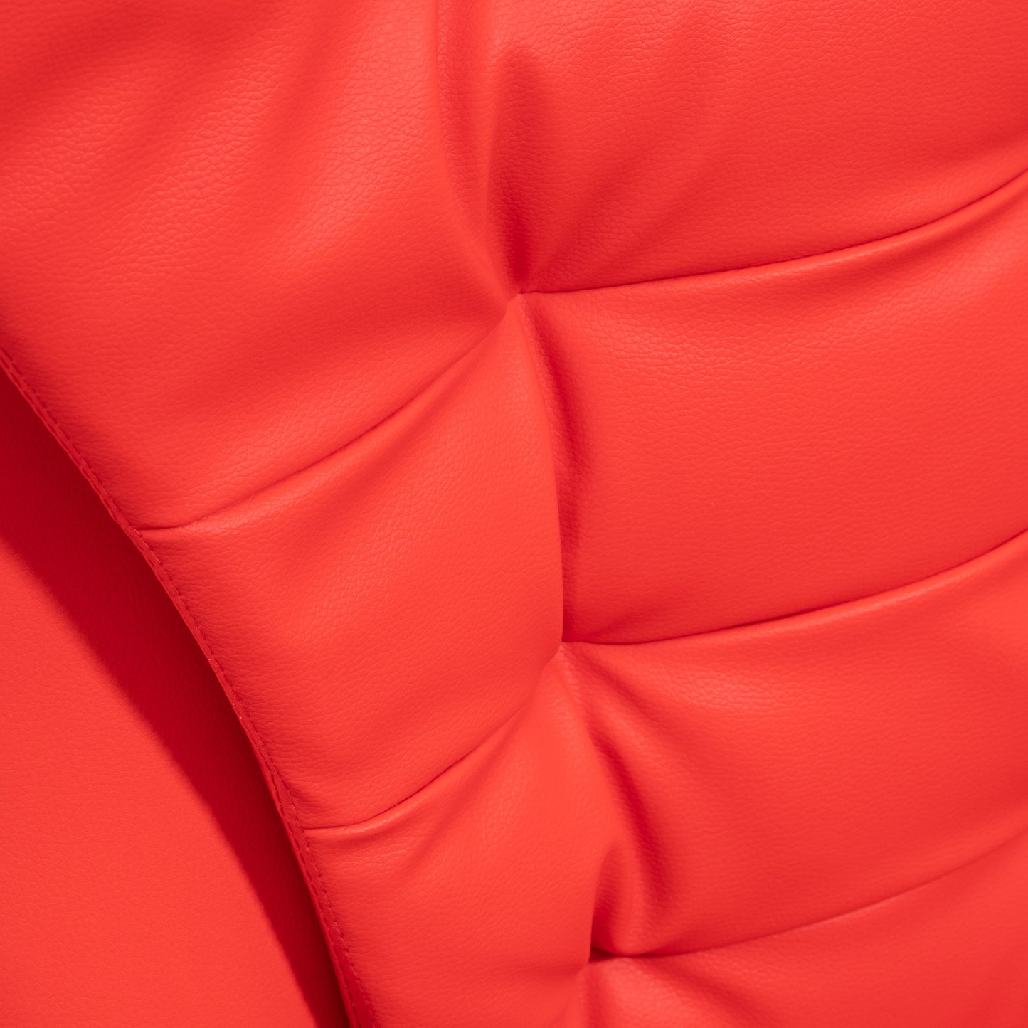 Closeup of a red faux leather tufted armchair showing texture and stitching