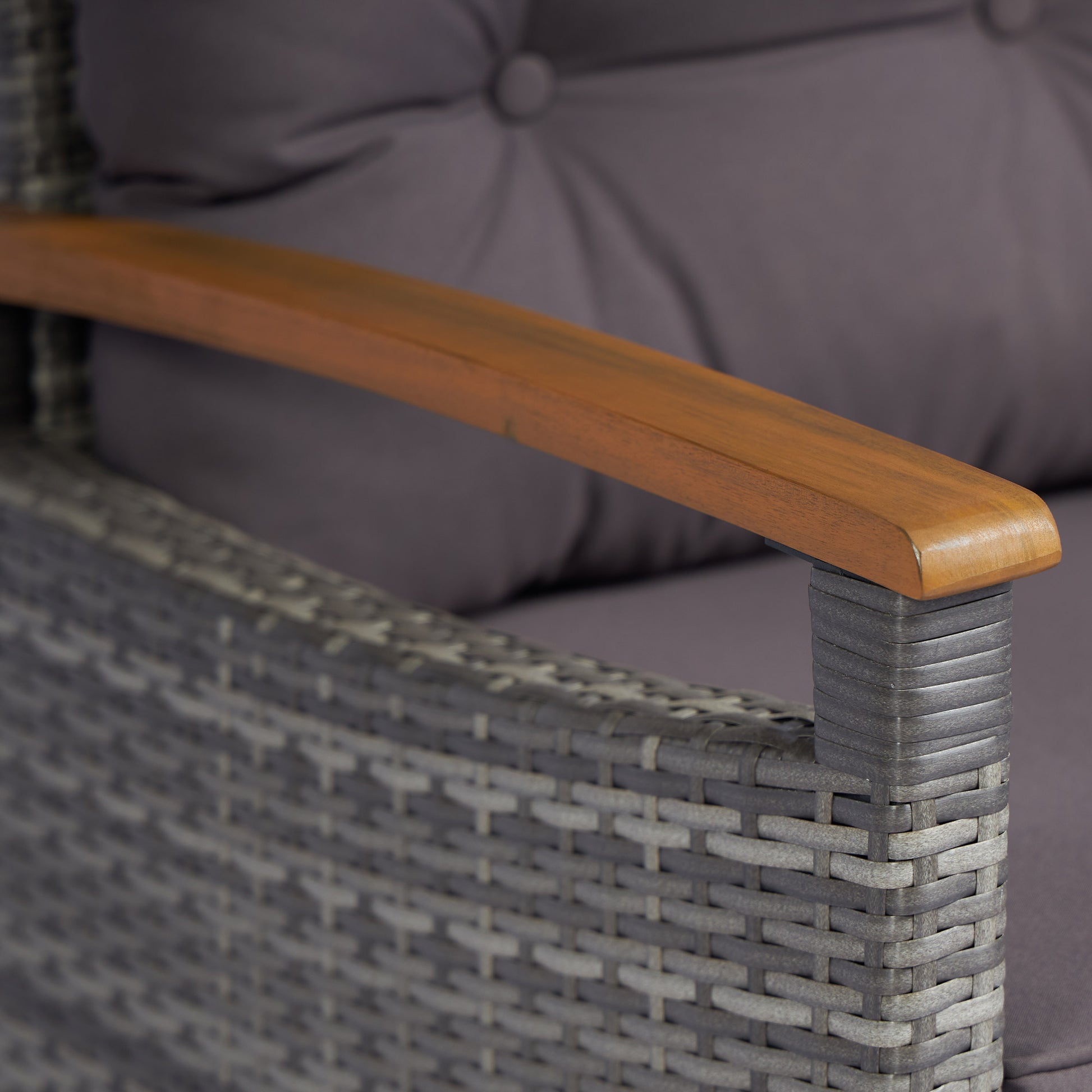 Closeup of a grey rattan armchair armrest with a wooden accent and cushion