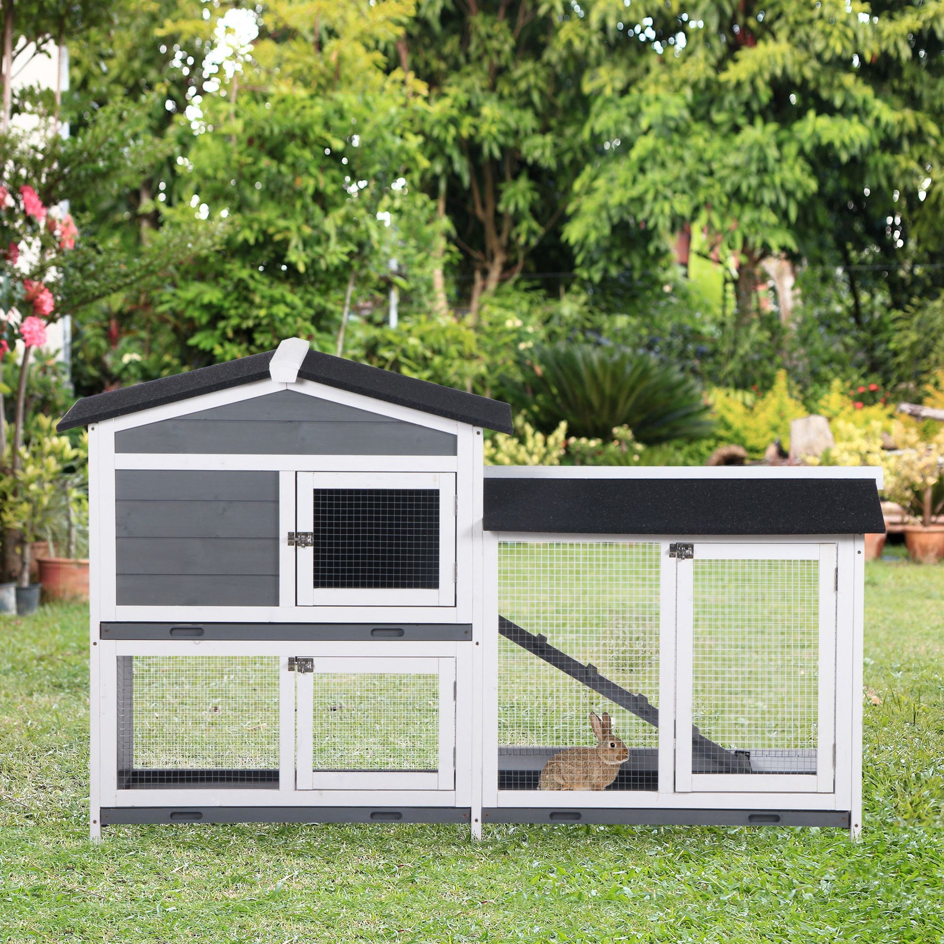 Gray and white wooden outdoor rabbit hutch with two levels and a small brown rabbit