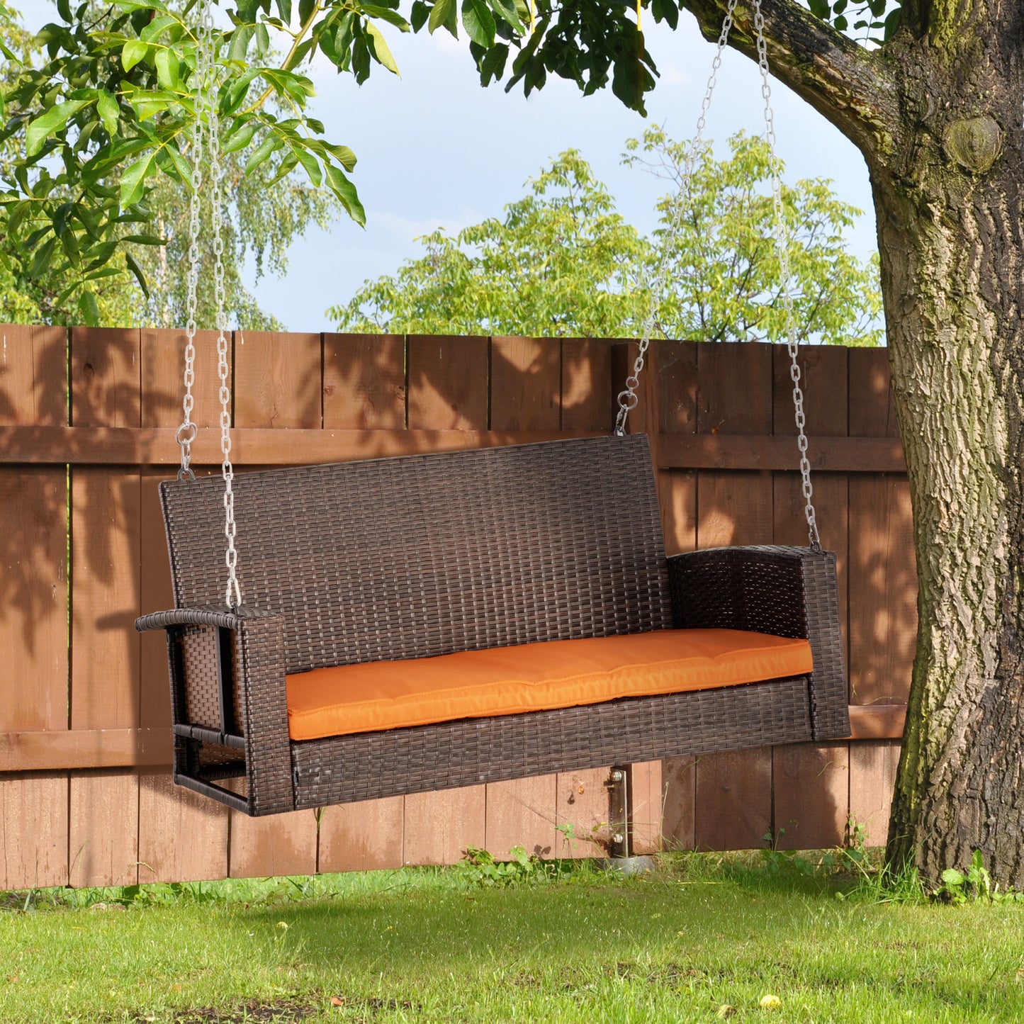Brown wicker porch swing with orange cushion hanging from tree