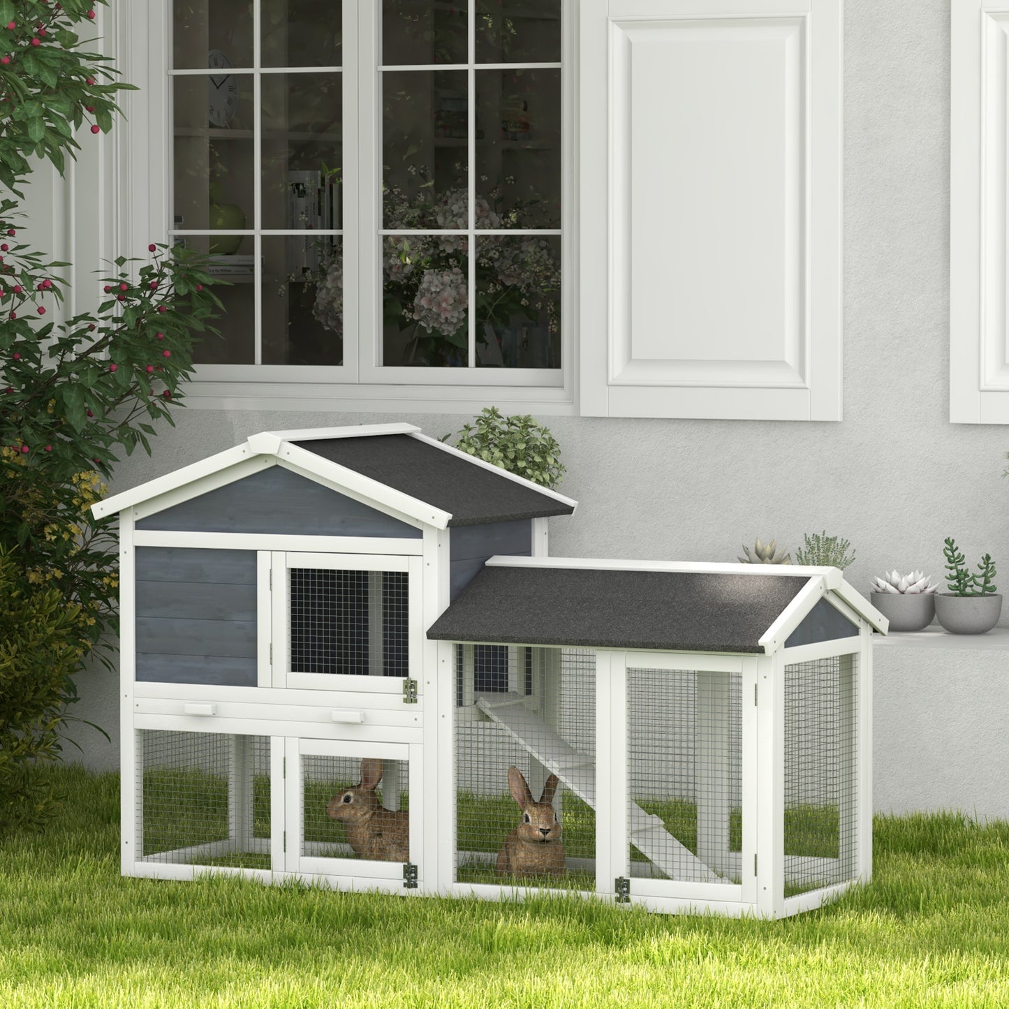 Twotier grey and white wooden rabbit hutch with two bunnies inside on a grassy lawn