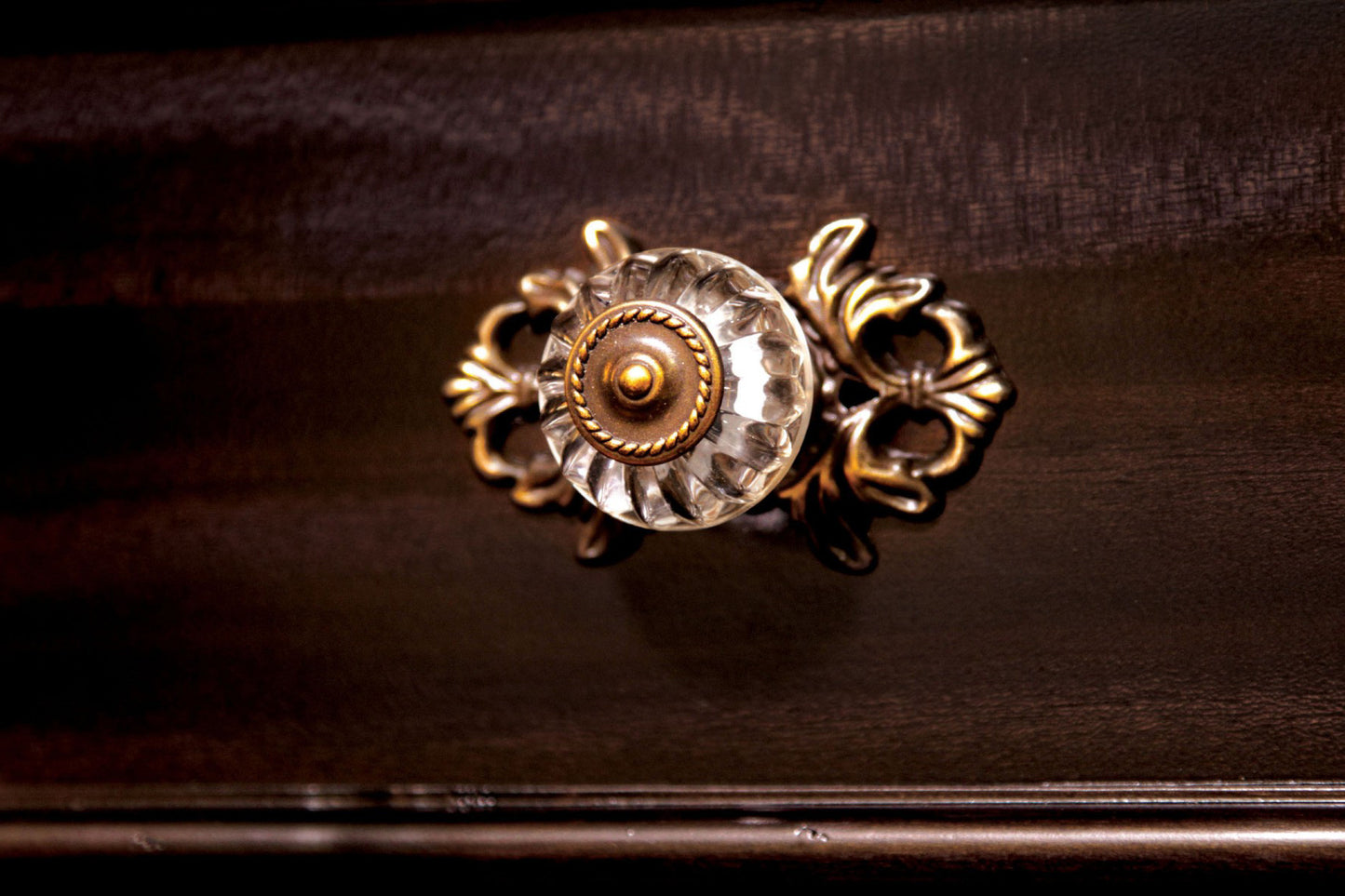 Antique glass drawer knob with ornate brass accents on dark wood