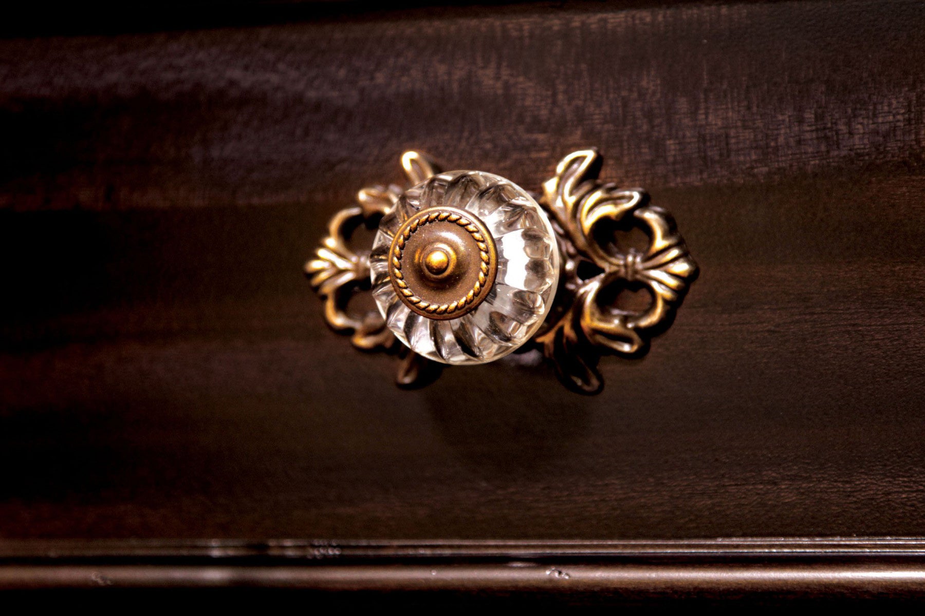 Antique glass drawer knob with ornate brass accents on dark wood