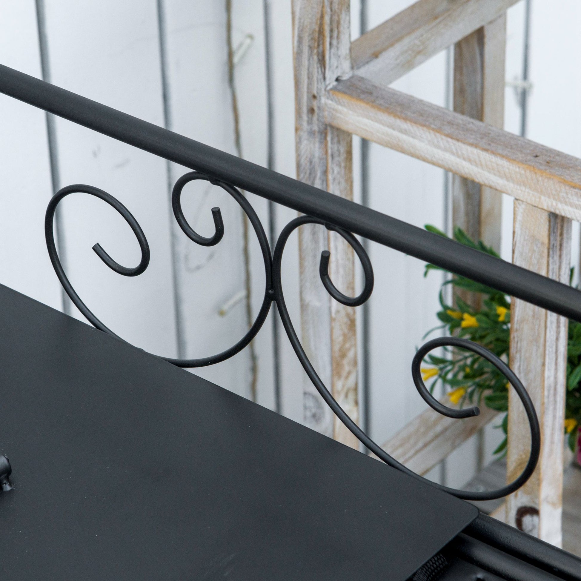 Black metal plant stand with decorative scrollwork and a rustic wooden ladder backdrop