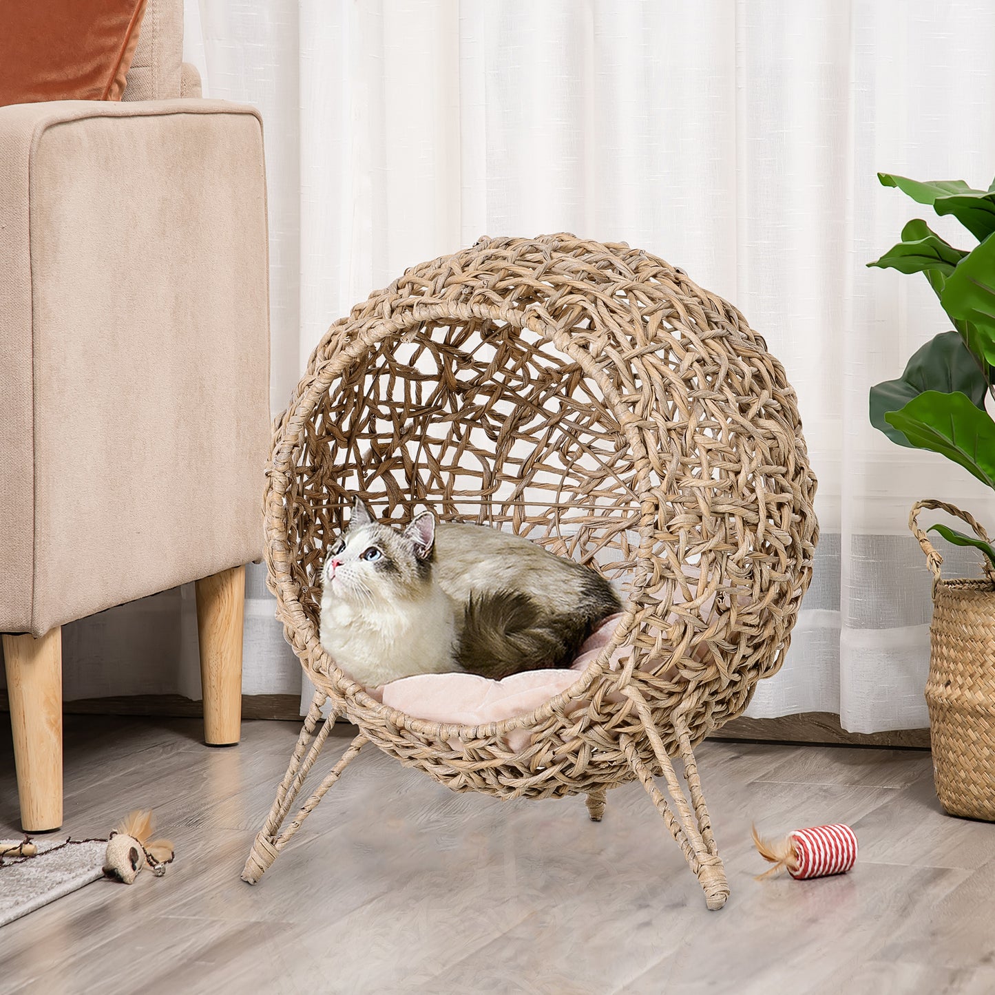 Round woven rattan cat bed with pink cushion and a Siamese cat resting inside