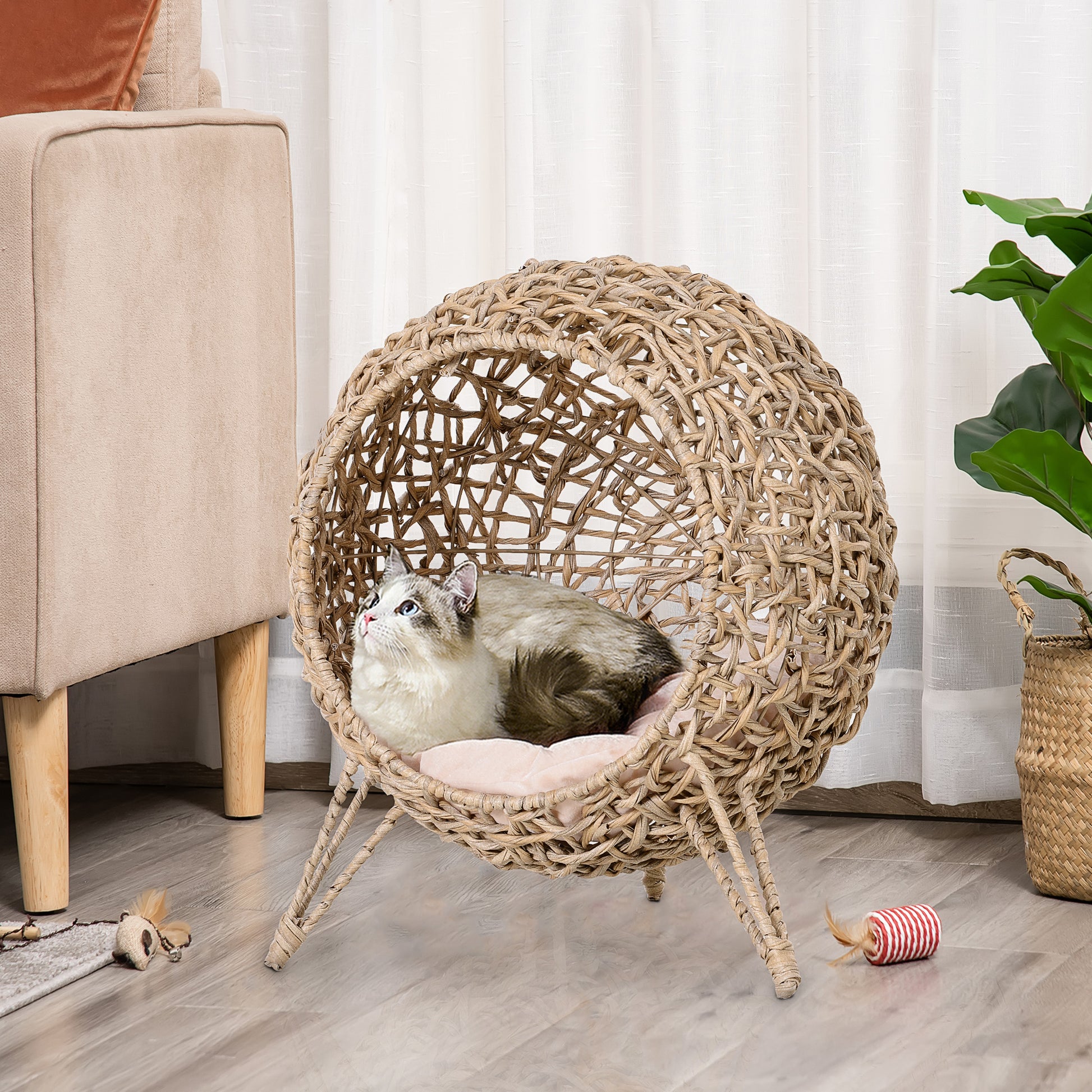 Round woven rattan cat bed with pink cushion and a Siamese cat resting inside
