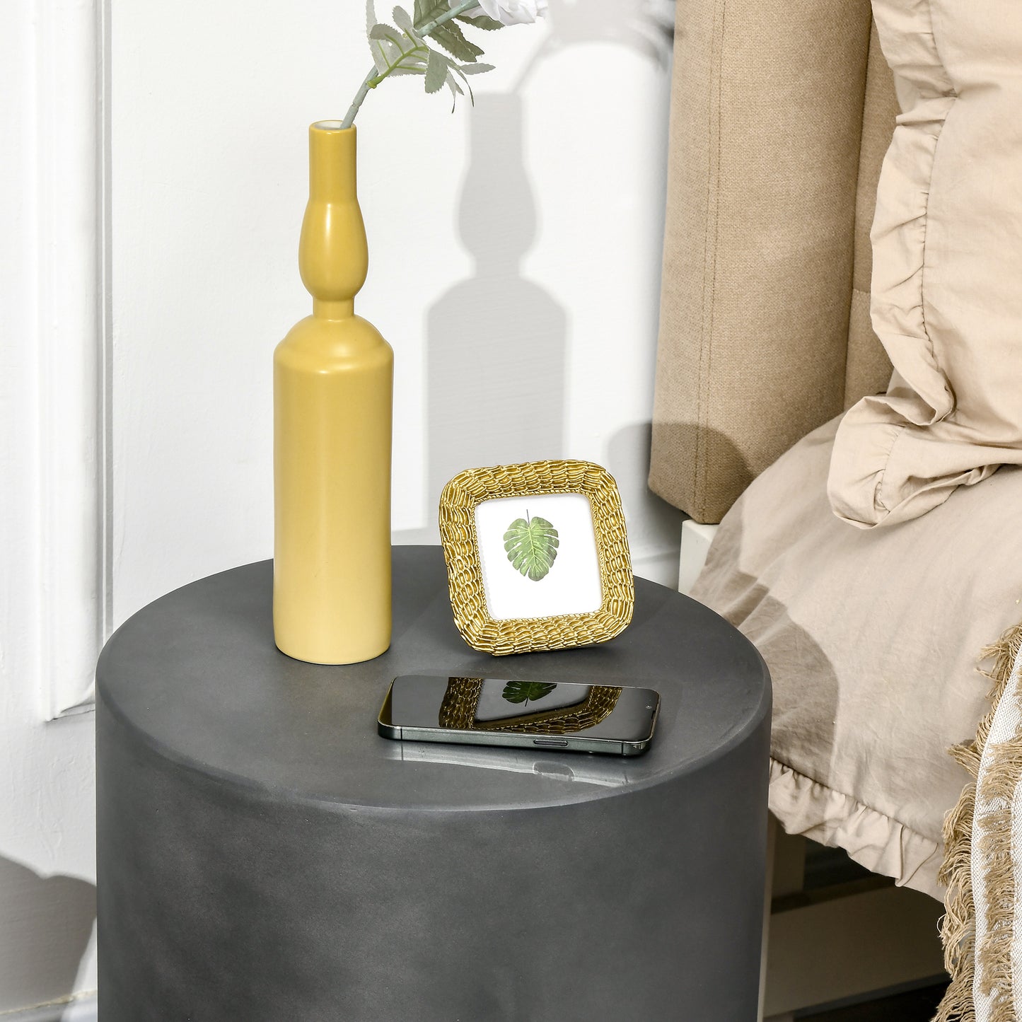 Matte grey cylindrical side table with a mustard yellow ceramic vase and gold picture frame