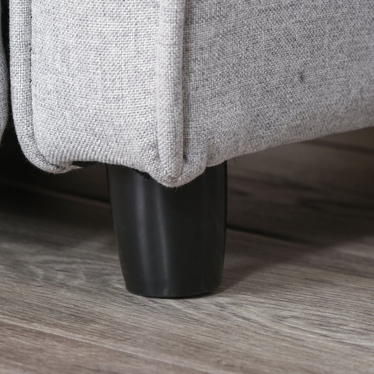 Closeup of grey fabric sofa corner with black tapered leg on woodlook floor
