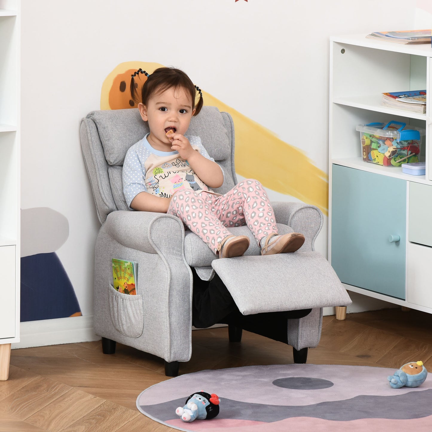 Gray fabric toddler recliner with footrest extended featuring side pocket with book