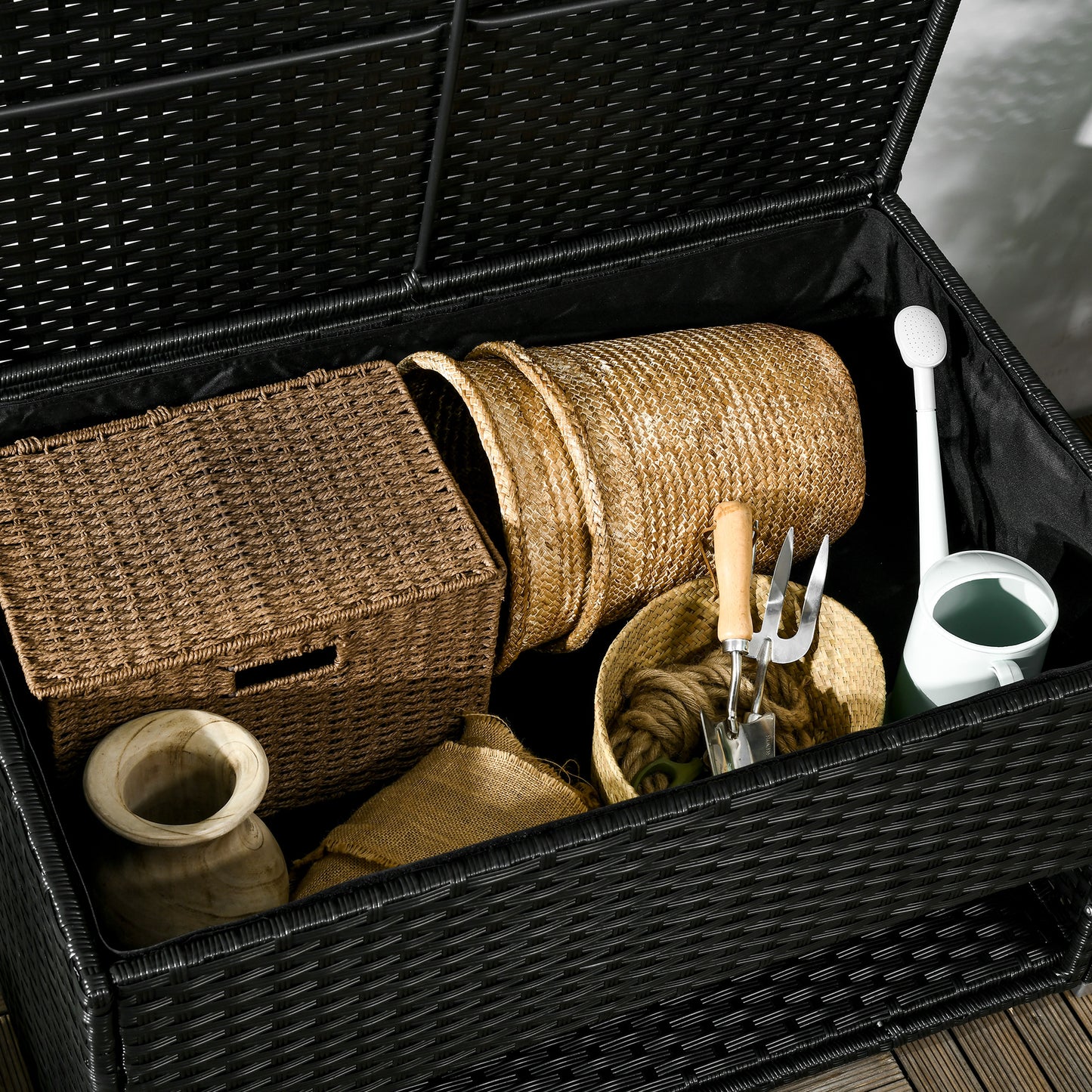 Woven black wicker outdoor storage box with gardening tools and watering can inside