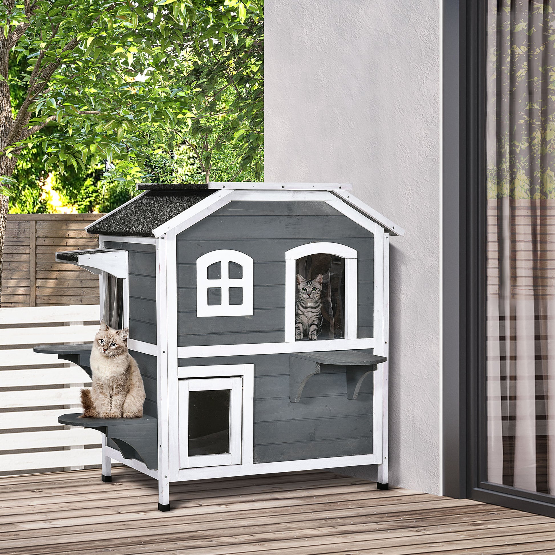 Gray wooden cat house with two levels and two cats lounging outside