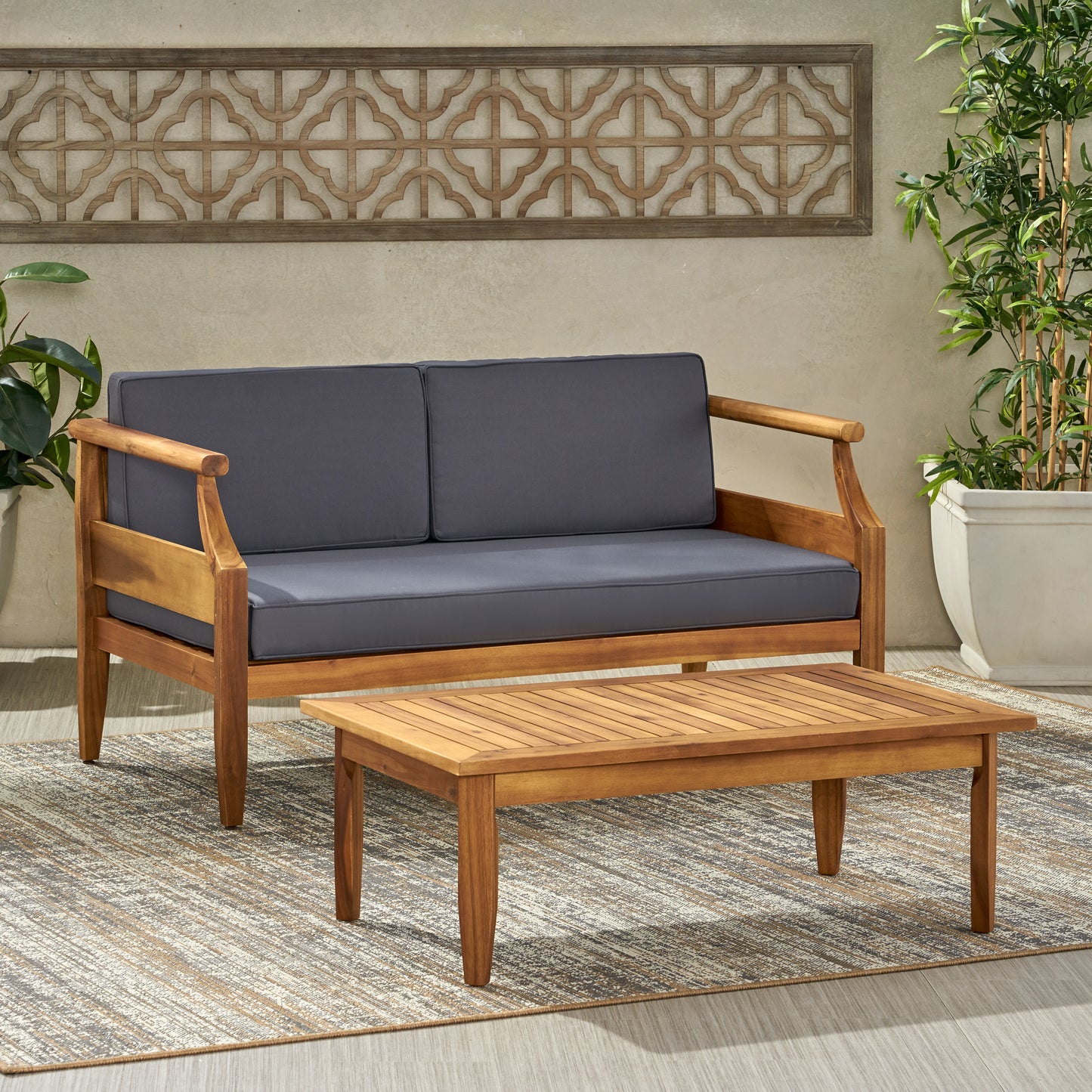 Twoseater patio sofa with charcoal grey cushions and a wooden frame paired with a matching coffee table
