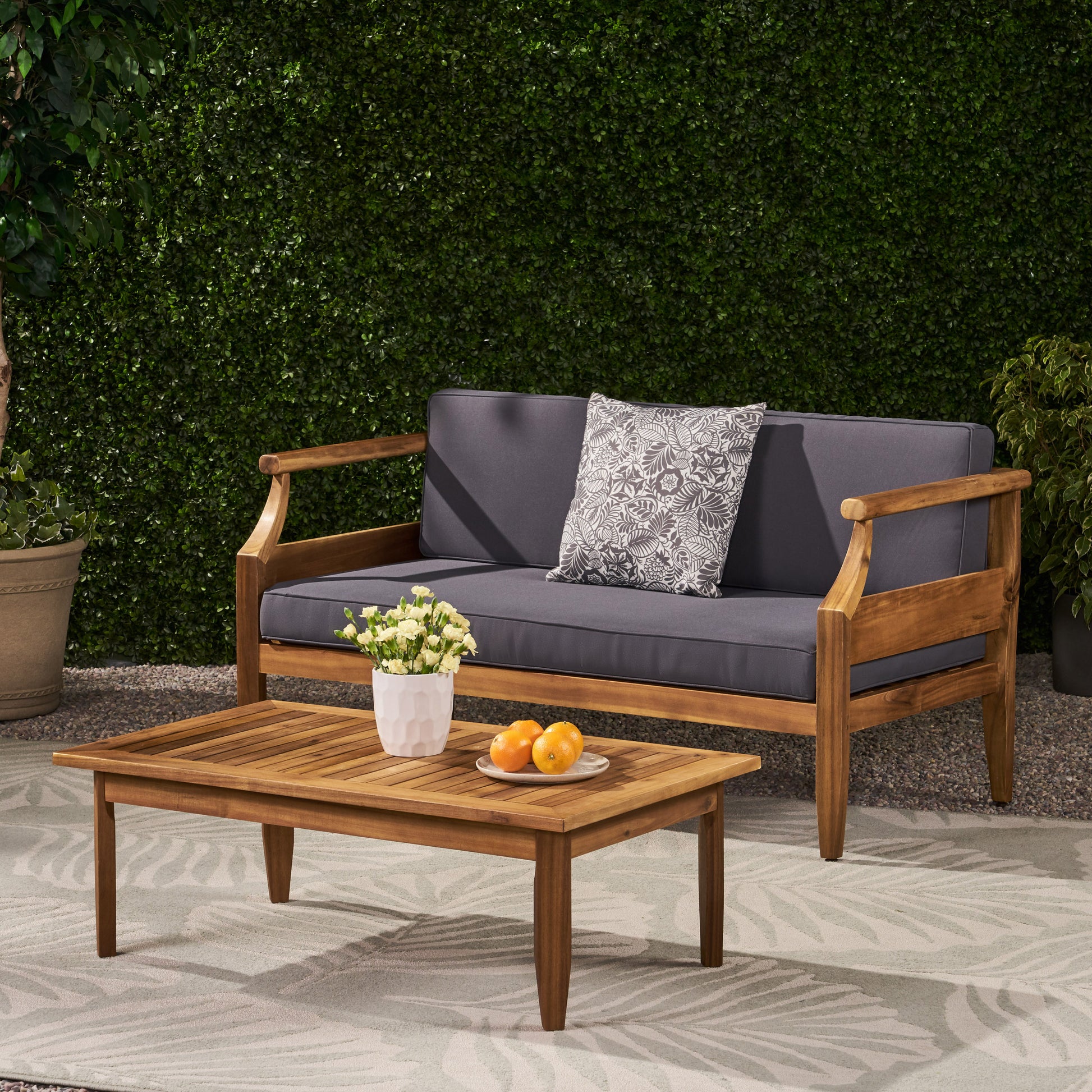 Acacia wood outdoor loveseat with gray cushions and patterned throw pillow