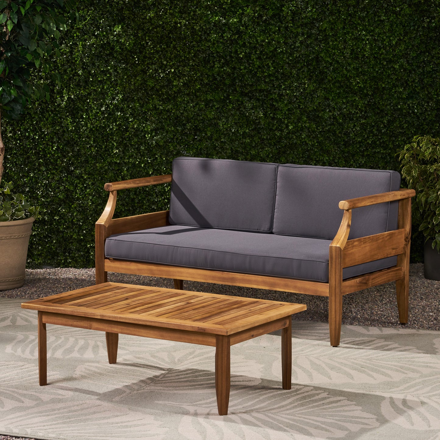 Acacia wood outdoor sofa with dark gray cushions on a patterned rug