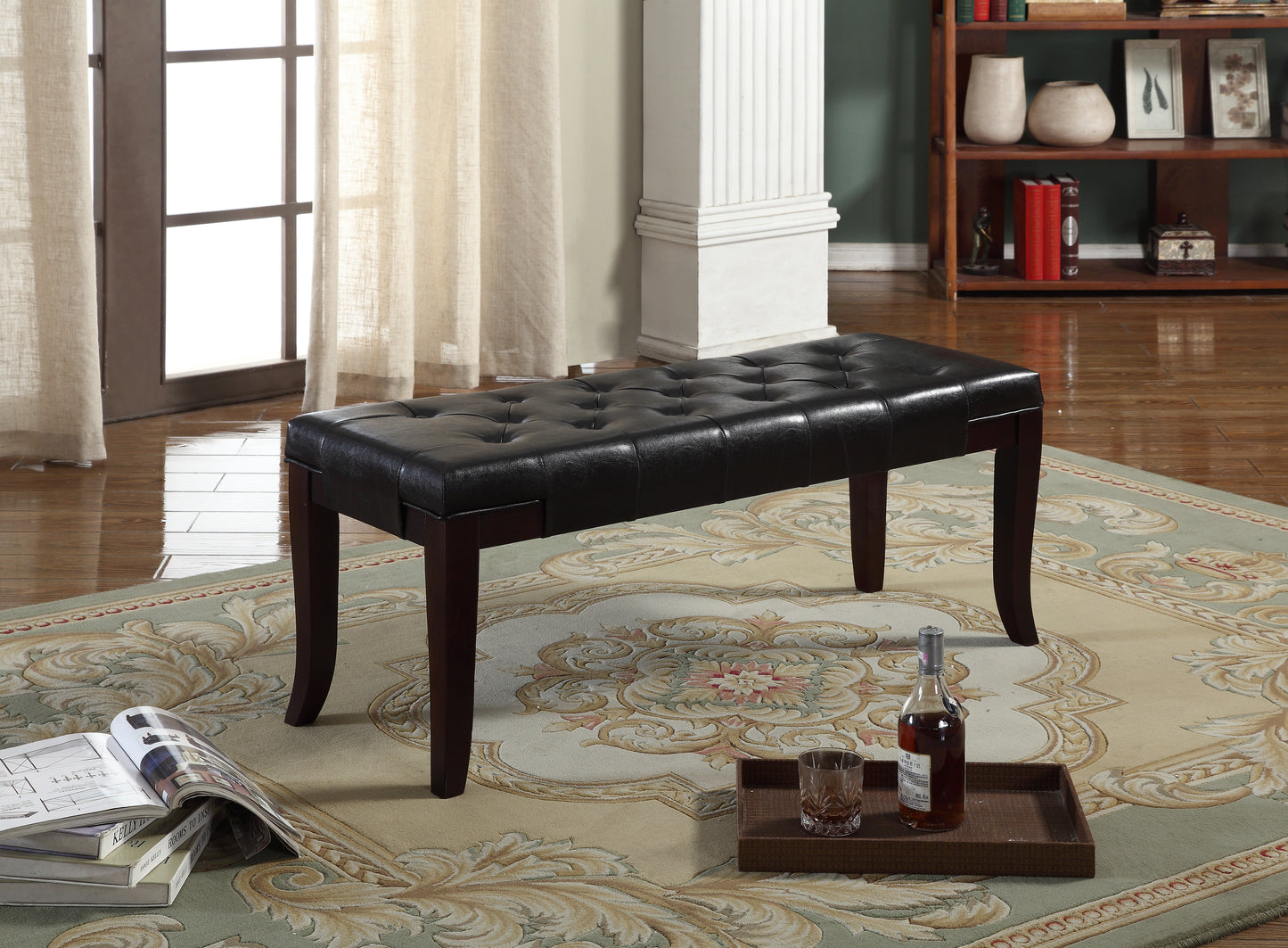 Black tufted leather ottoman bench with dark wood legs on ornate rug