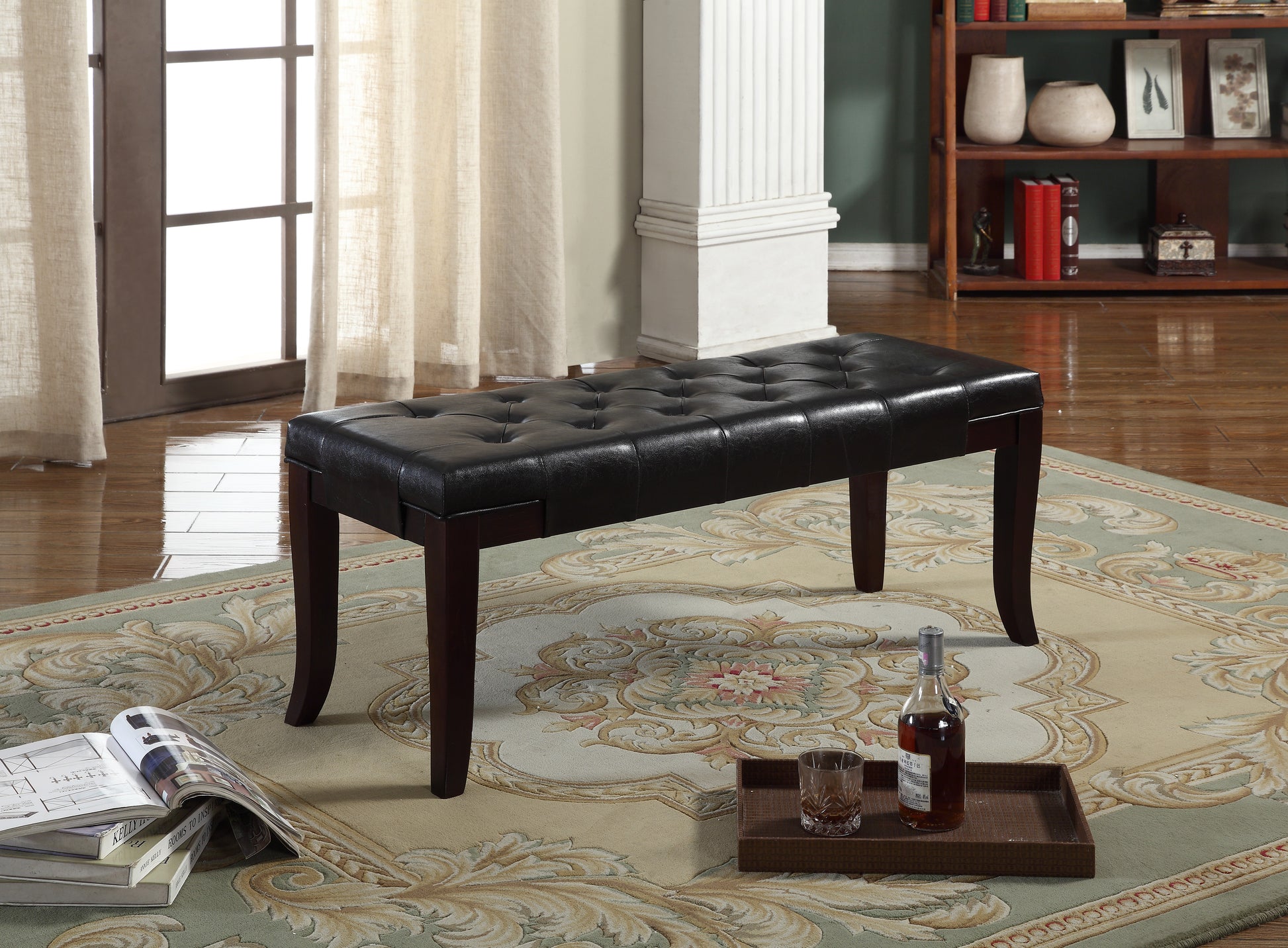 Black tufted leather ottoman bench with dark wood legs on ornate rug