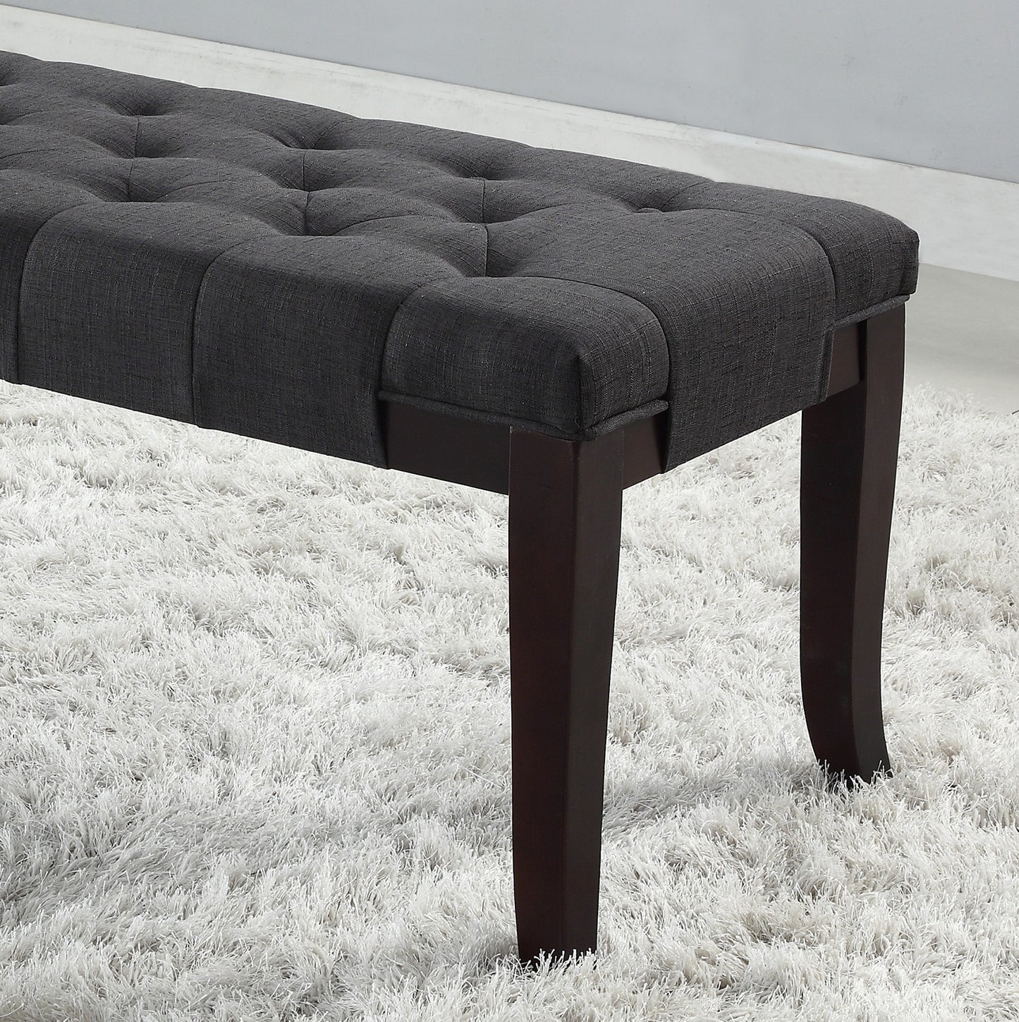Dark gray linen tufted bench with dark wood legs on a white shag rug
