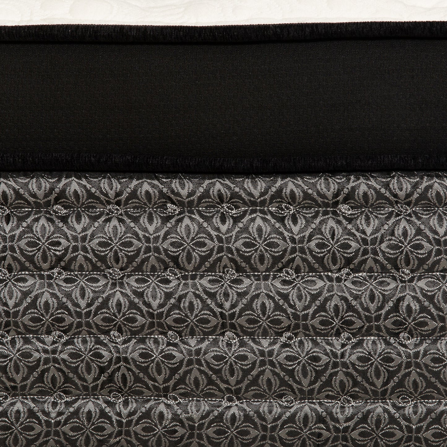 Closeup of a black mattress with a silver damask pattern on quilted fabric