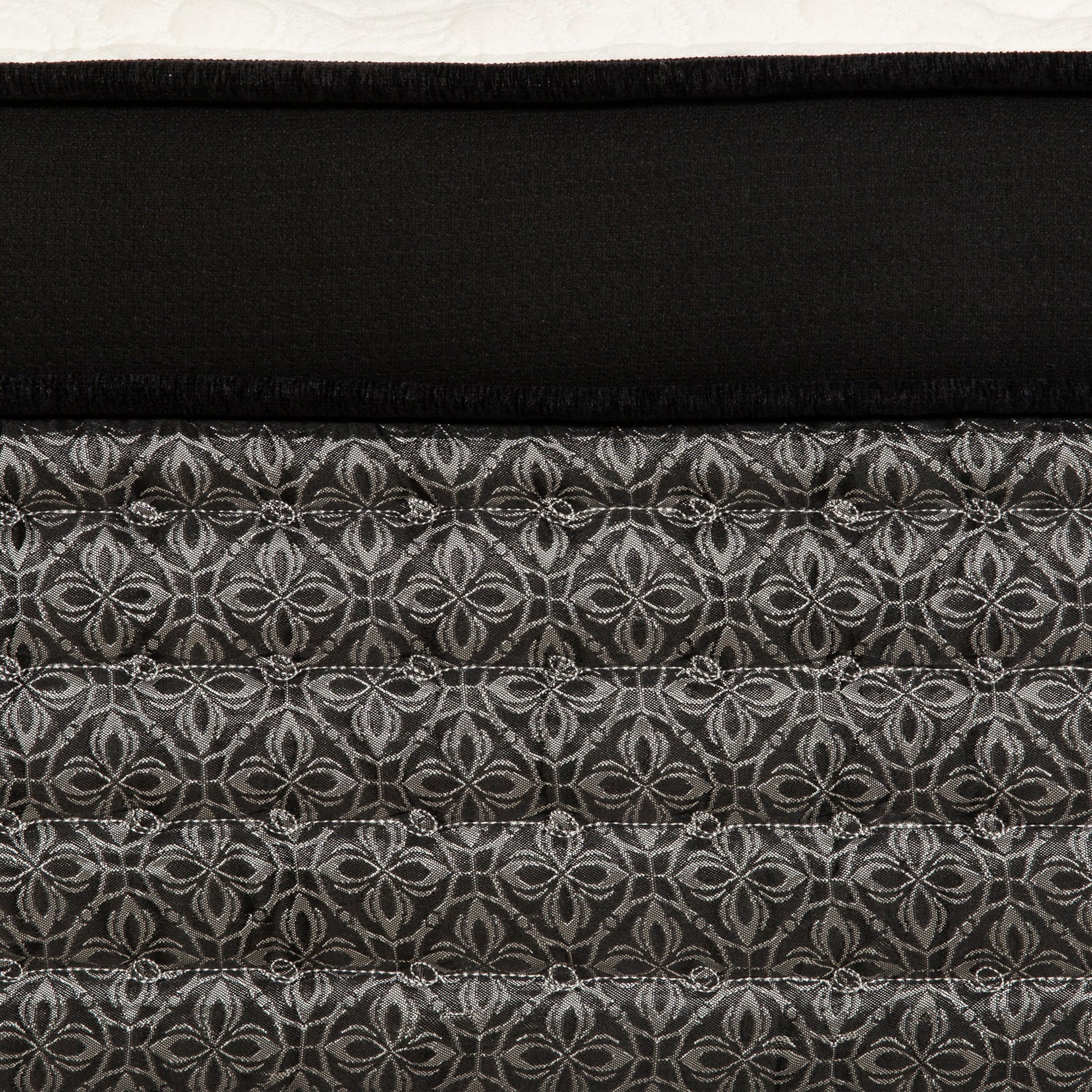 Closeup of a black mattress with a silver damask pattern on quilted fabric