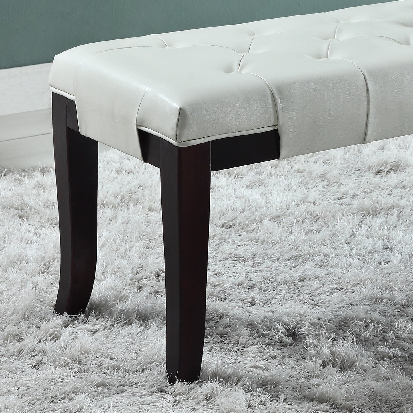 White faux leather tufted bench with dark wood legs on shag carpet