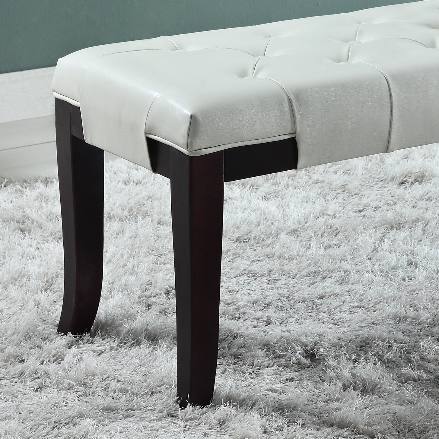 White faux leather tufted bench with dark wood legs on shag carpet