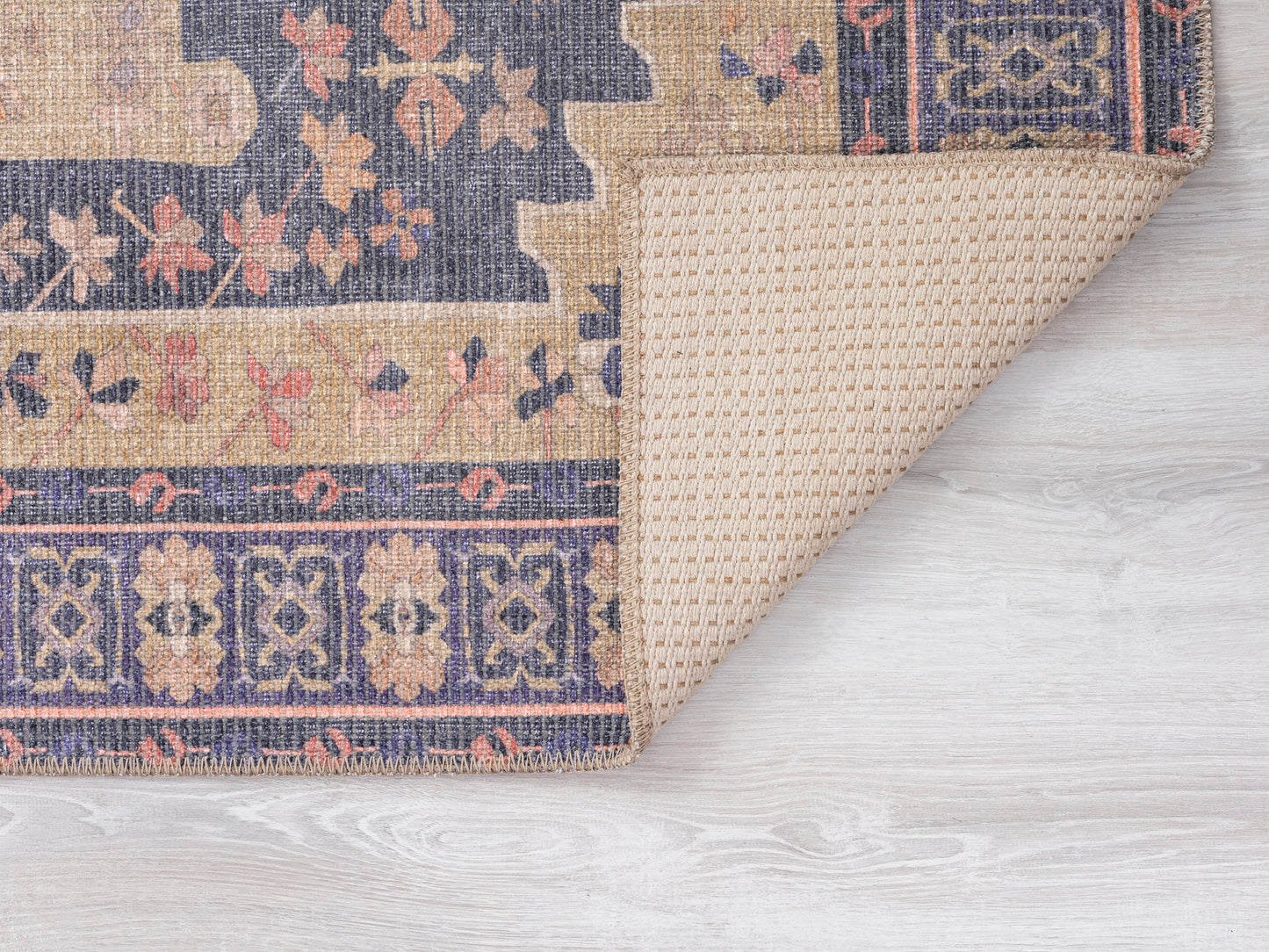 Closeup of a woven rug featuring floral patterns in navy tan and coral hues on a light wooden floor