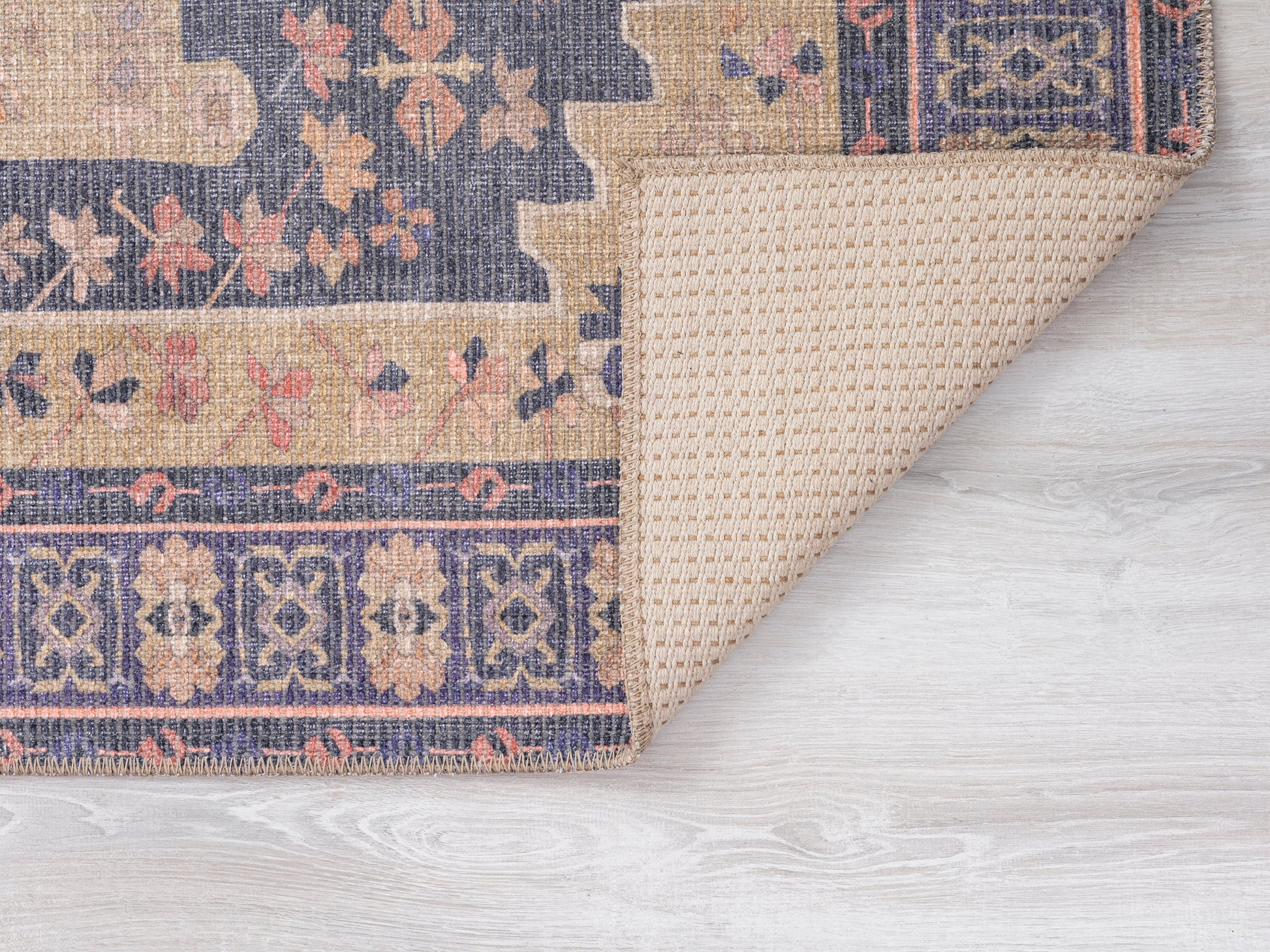 Closeup of a woven rug featuring floral patterns in navy tan and coral hues on a light wooden floor