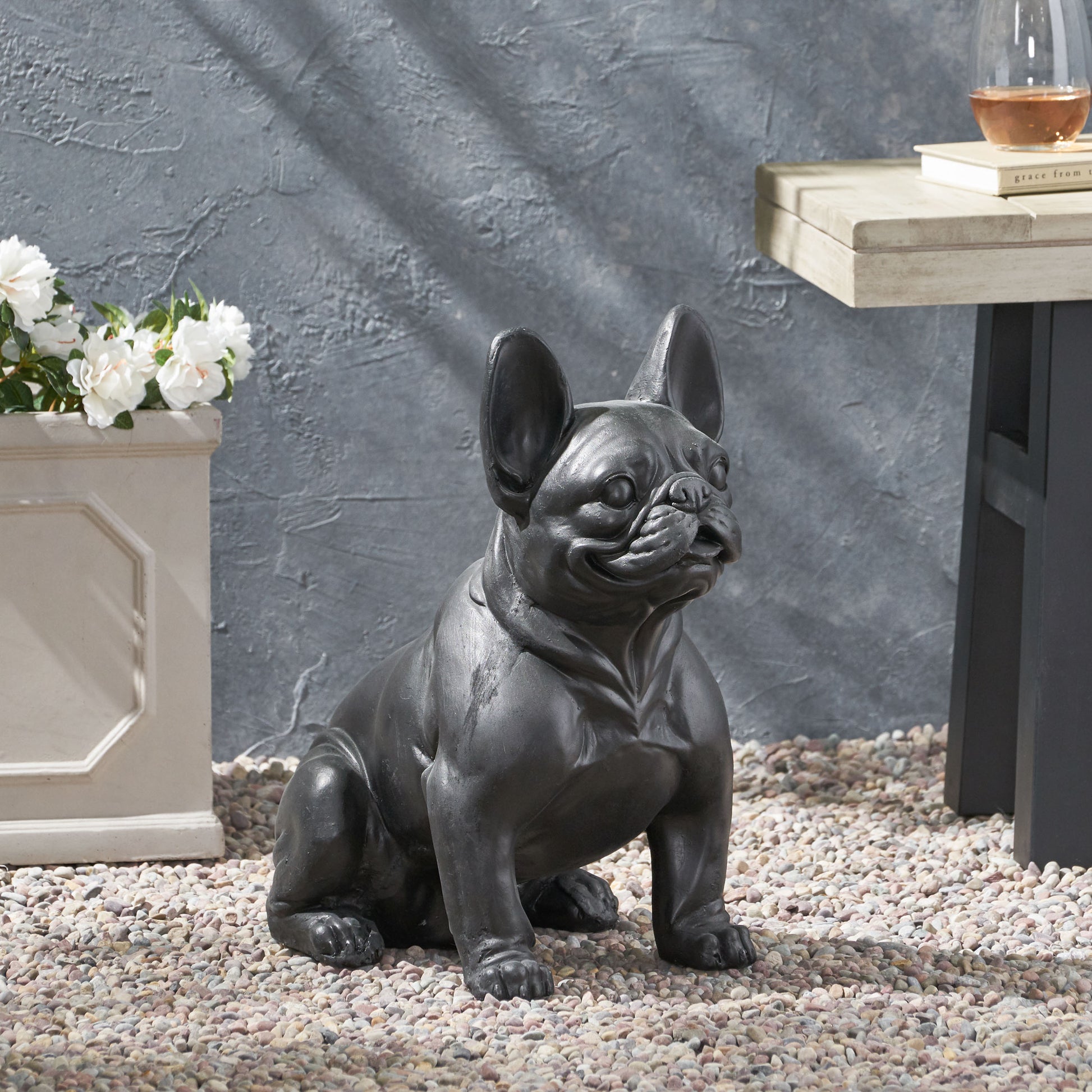 Dark gray French bulldog garden statue sitting on pebbles adding charm to outdoor spaces