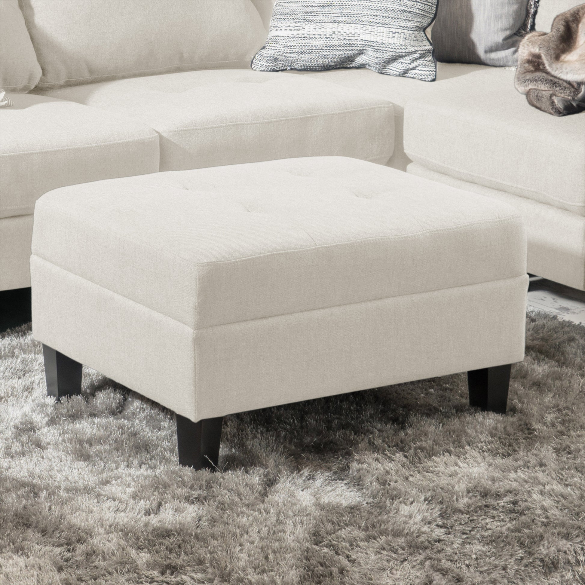 Cream upholstered ottoman with tufted top and dark wood legs on shag rug