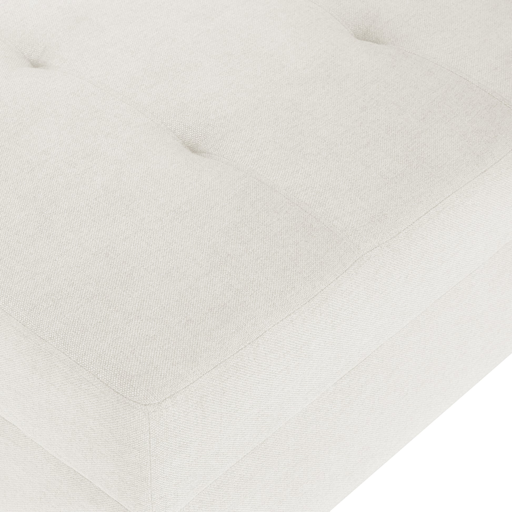 Closeup of a creamcolored linen tufted ottoman showing textured fabric and stitching detail