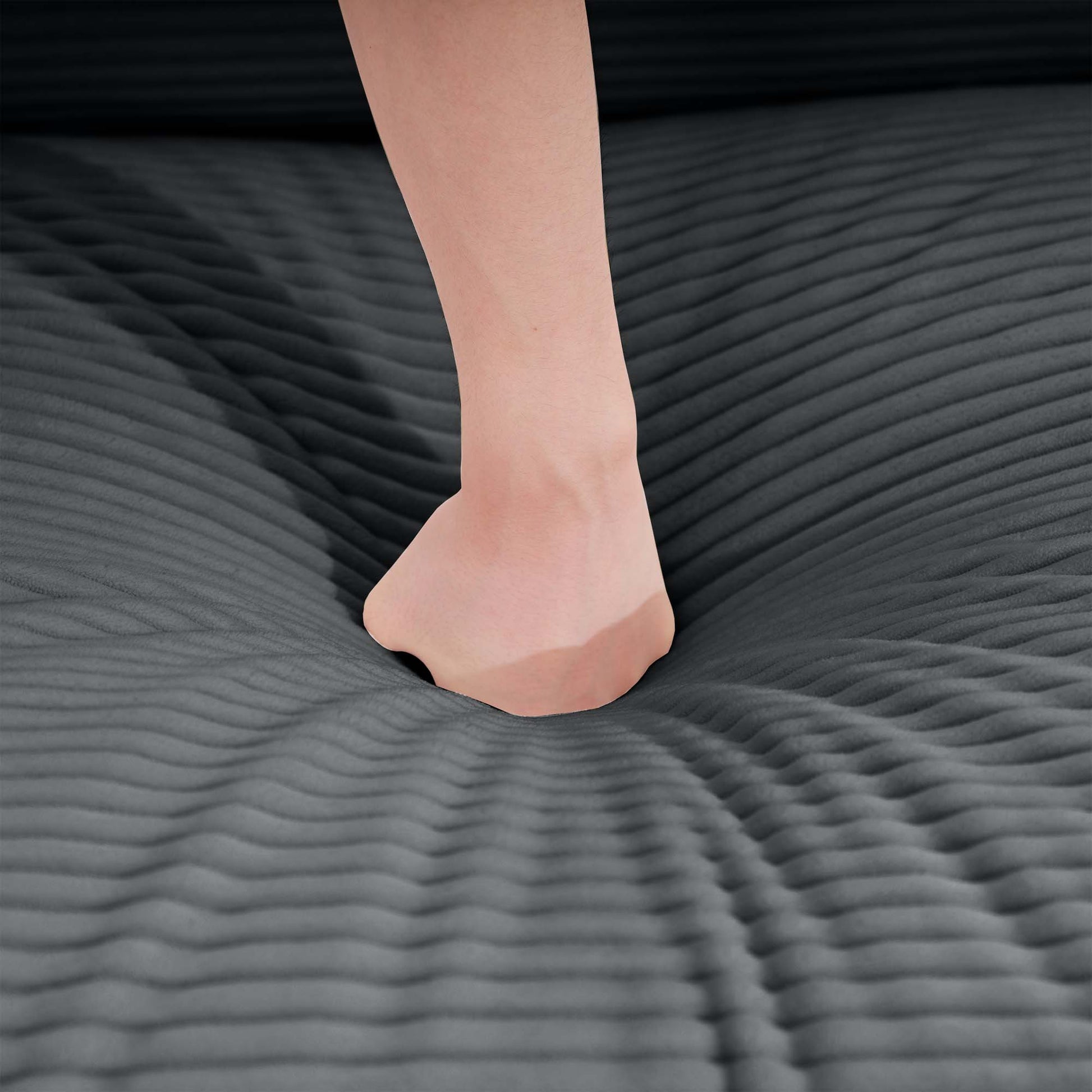 Closeup of a foot sinking into a plush charcoal gray corduroy sofa cushion highlighting comfort and texture
