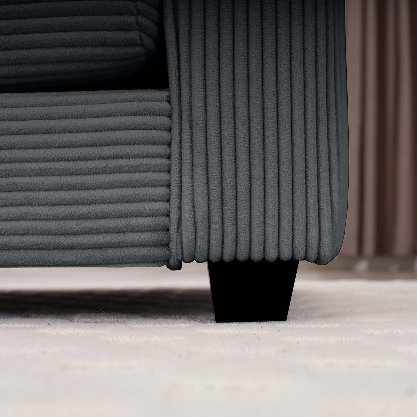 Closeup of a charcoal grey corduroy sofas textured fabric and black tapered leg