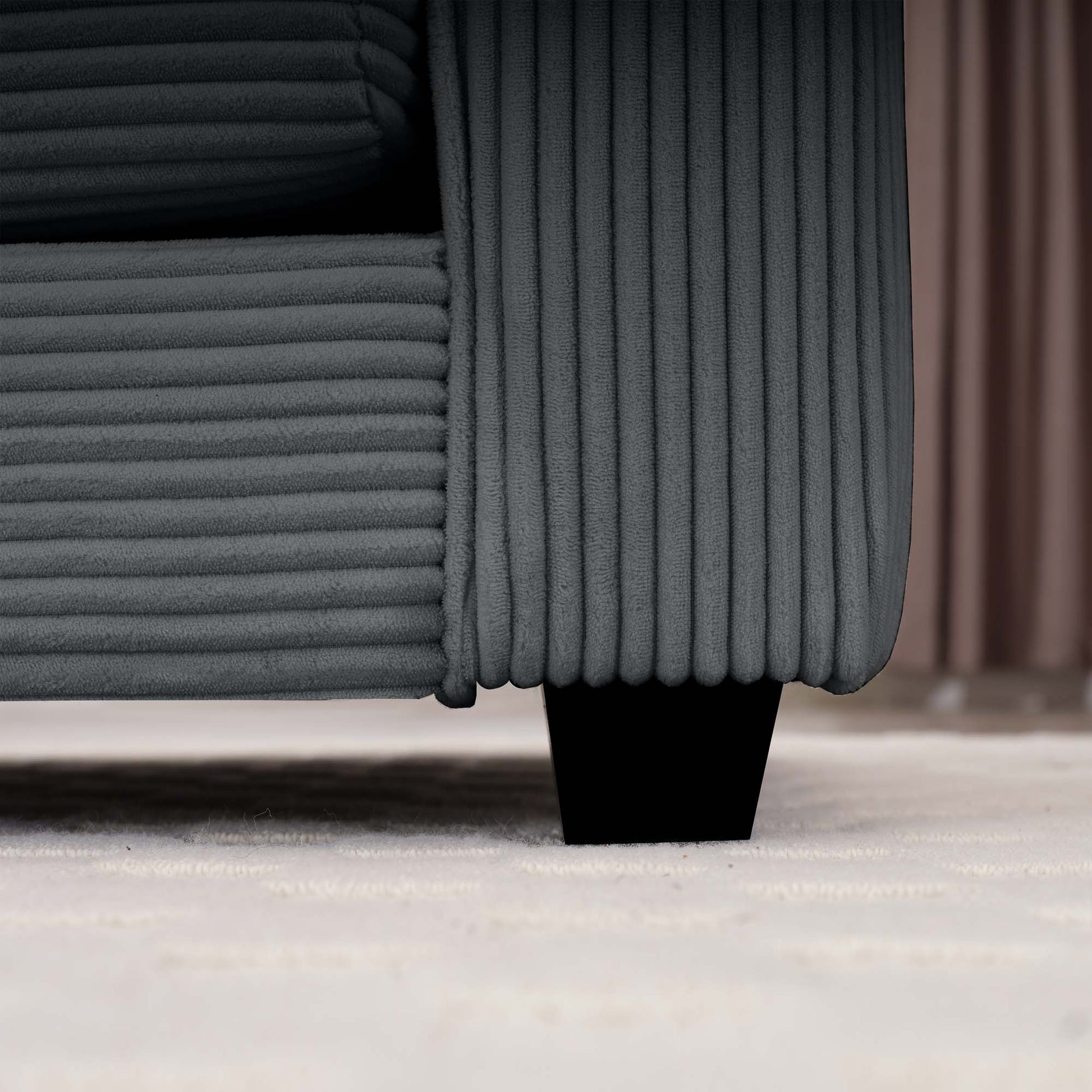 Closeup of a charcoal grey corduroy sofas textured fabric and black tapered leg