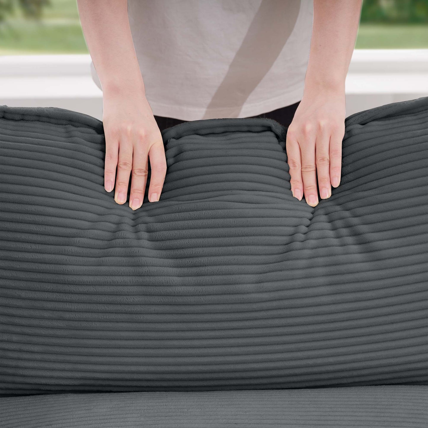 Closeup of hands pressing into plush grey corduroy sofa cushion showing texture