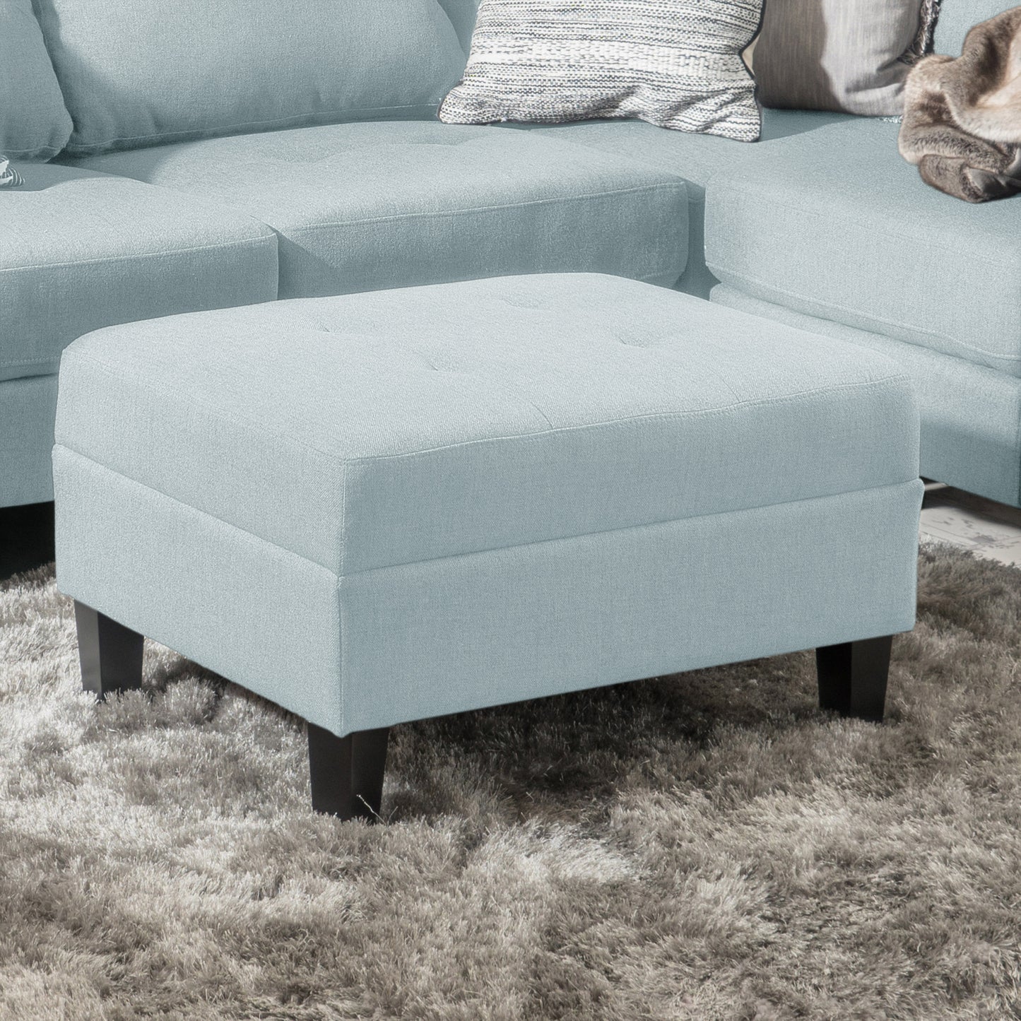 Sky blue fabric ottoman with tufted top on a plush gray rug